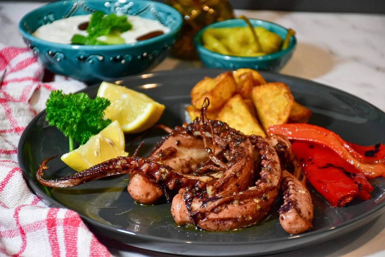 Gegrilde octopus met gebakken aardappelen, geroosterde paprika, citroen en peterselie op een donker bord