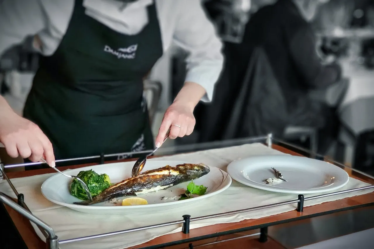 Ober fileert een gegrilde hele vis met citroen en groenten op een bord in een restaurant