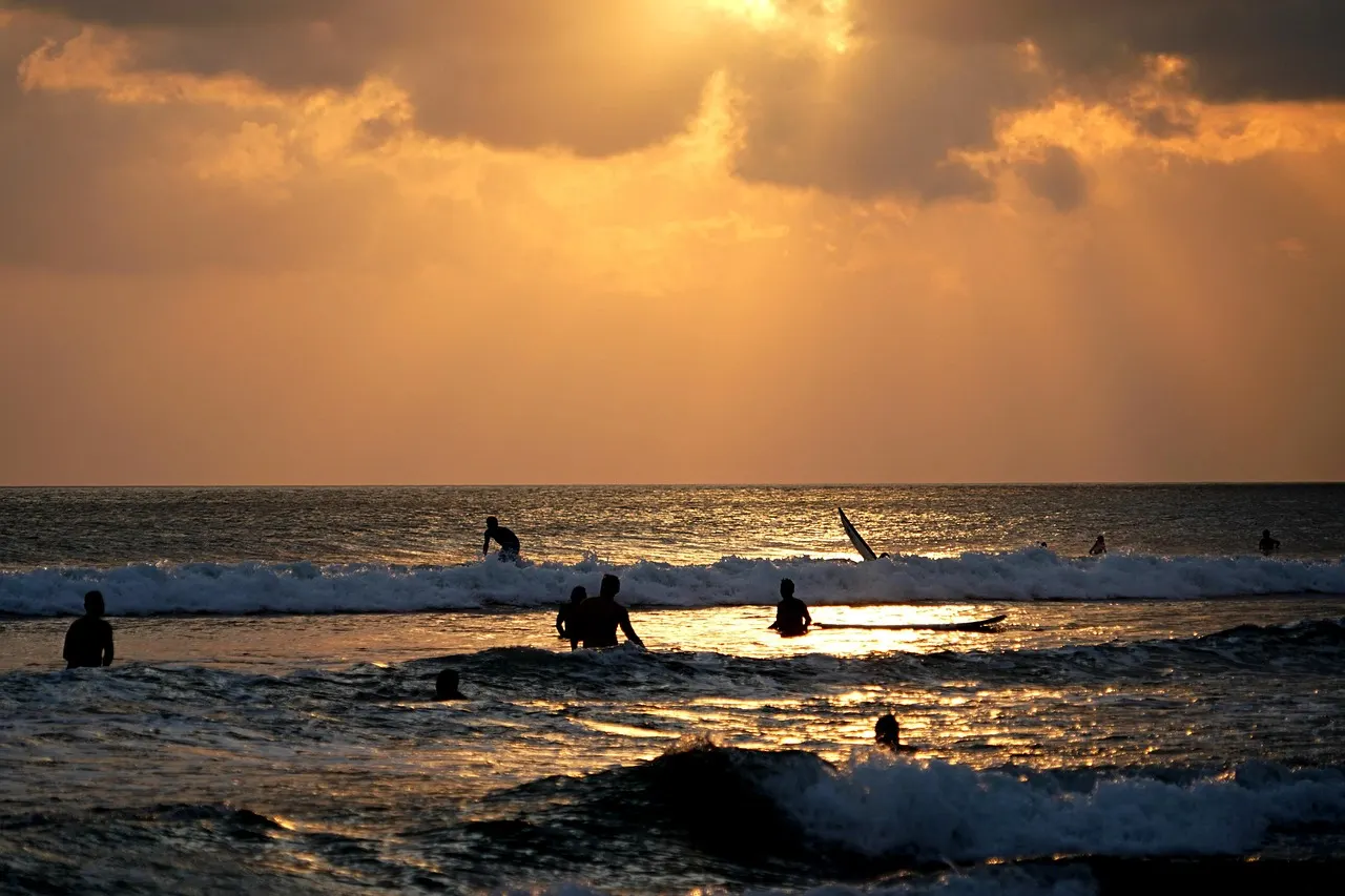 Surfers en zwemmers in de golven bij een goudkleurige zonsondergang op Kuta strand