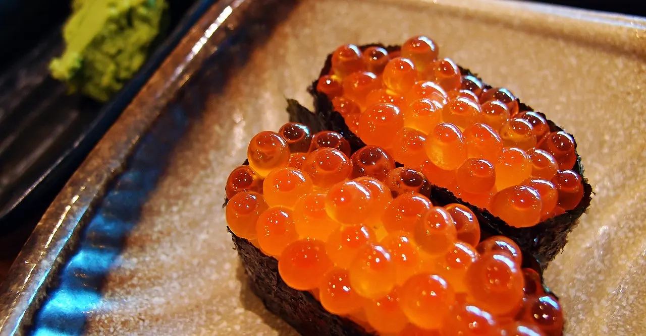 Ikura-sushi met glanzende oranje zalmeitjes en nori op een bord, met wasabi op de achtergrond