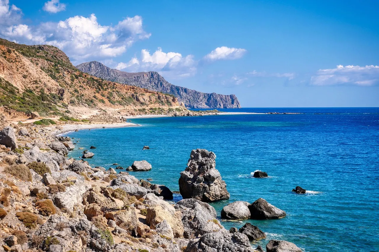 Rotsachtige kust van Kreta met helderblauwe zee, een baai en bergen onder een blauwe lucht