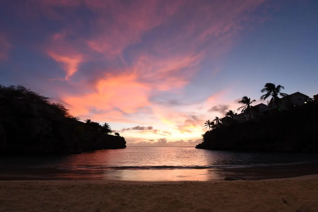Zonsondergang boven de baai van Playa Lagun met kliffen, palmbomen en een zandstrand op de voorgrond