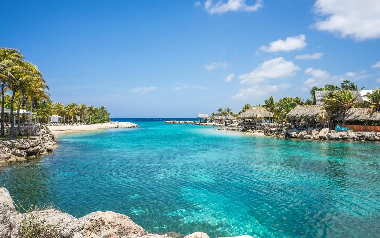 Turquoise lagune met palmbomen, strand en rieten parasols aan de kust bij Mambo Beach op Curaçao
