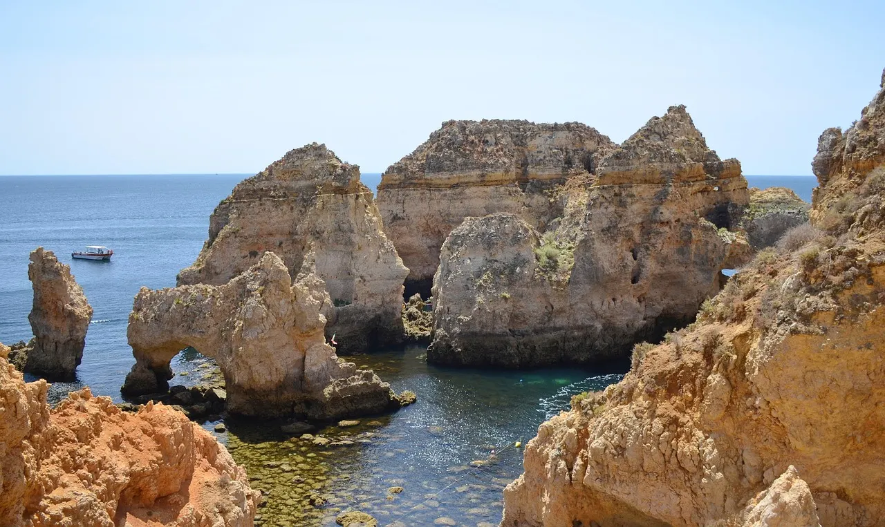 Goudgele rotsformaties met natuurlijke boog in helderblauw zeewater bij Ponta da Piedade, met een bootje op zee