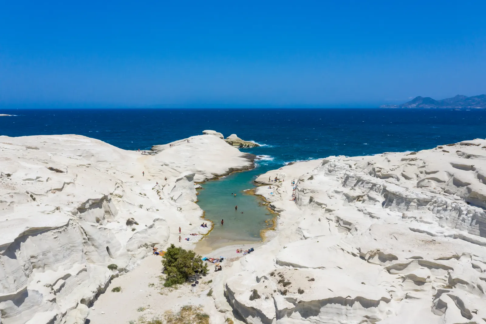 Luchtfoto van Sarakiniko met witte vulkanische rotsen rond een smalle turquoise inham en diepblauwe zee