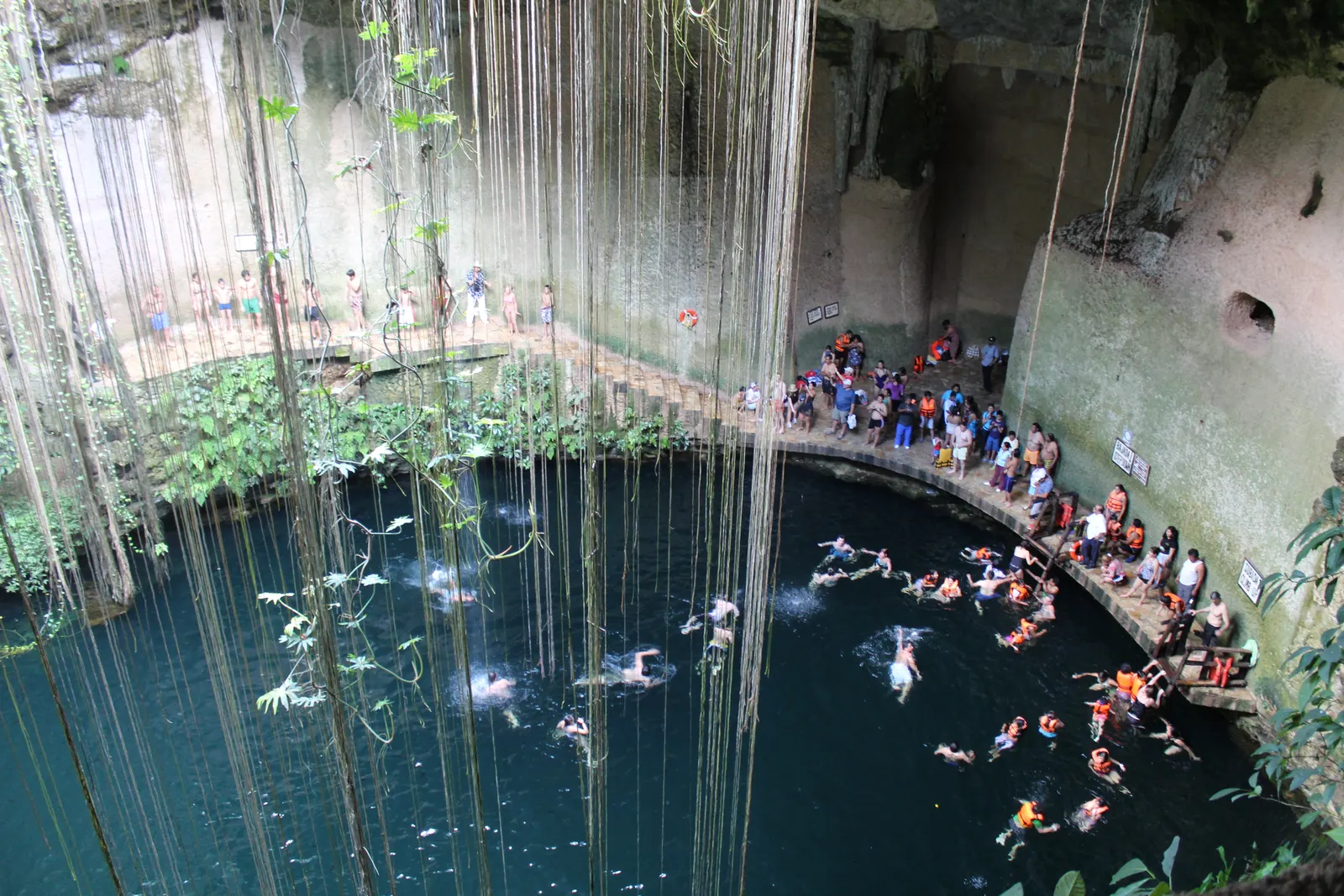 Cenote Ik Kil van bovenaf gezien met hangende lianen boven het diepblauwe water en zwemmende bezoekers