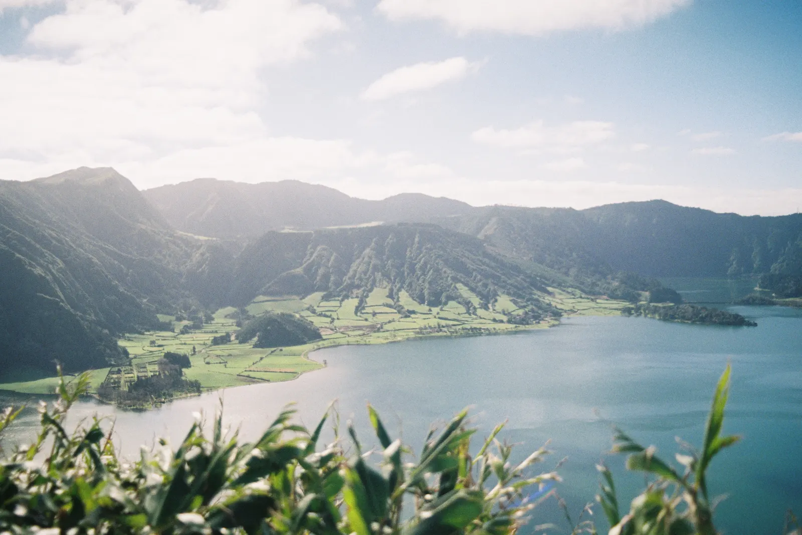 Kratermeer omringd door groene bergwanden en weilanden onder een zonnige hemel op São Miguel, Azoren
