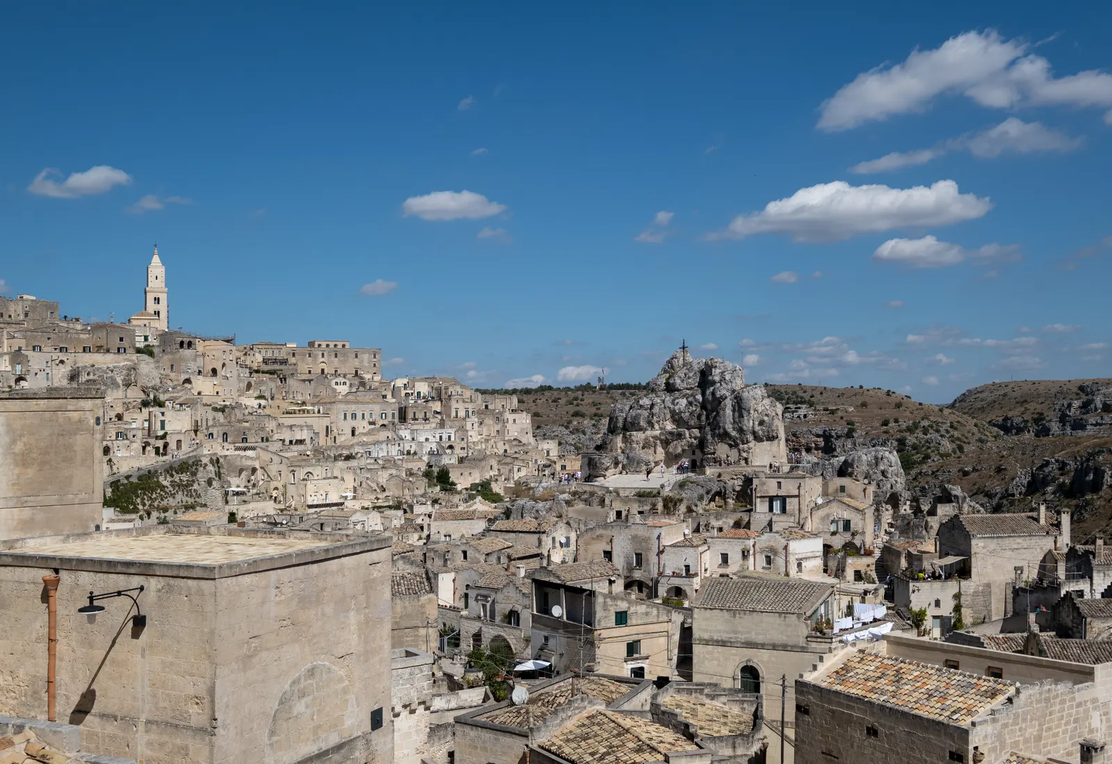 Uitzicht over de stenen huizen van de Sassi van Matera met de klokkentoren van de kathedraal onder een blauwe lucht