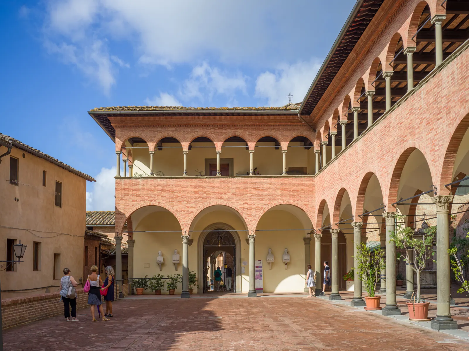 Binnenplaats van het Santuario di Santa Caterina in Siena met bakstenen arcaden en loggia's onder blauwe lucht