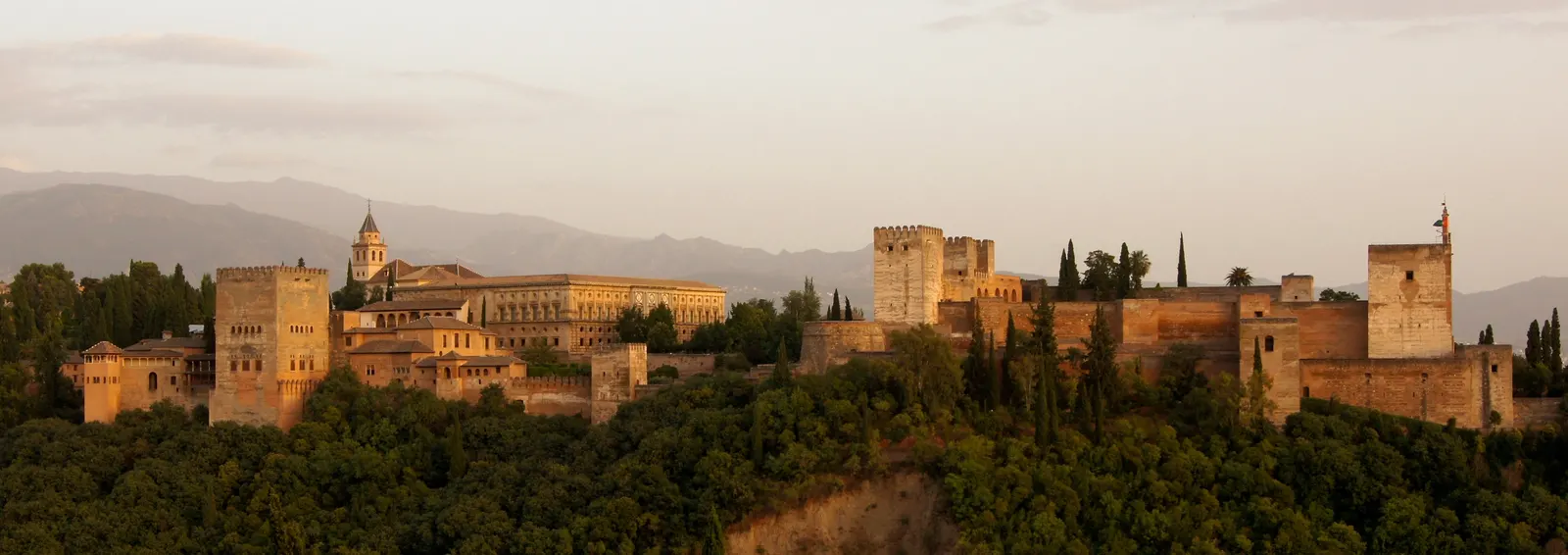 Het Alhambra-complex op een heuvel in Granada bij zonsondergang, met de bergen op de achtergrond