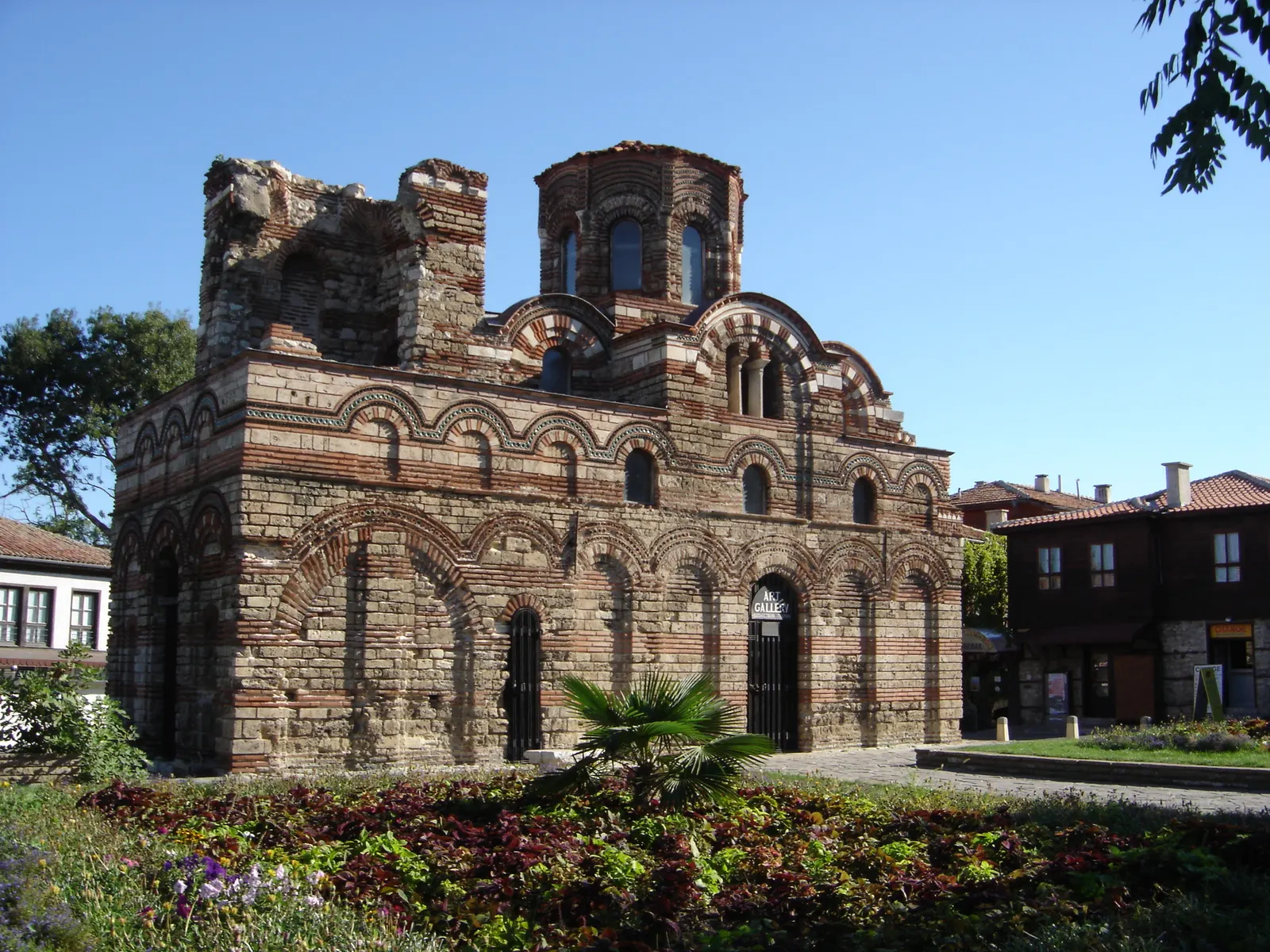 Gevel van de Kerk van Christus Pantocrator in Nessebar met rood-witte bakstenen bogen onder een blauwe lucht