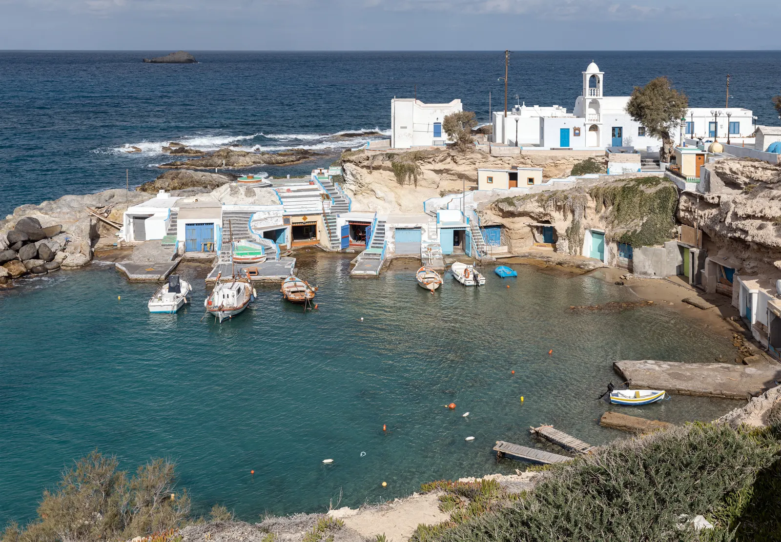 Vissersdorp Mandrakia op Milos met kleurrijke botenhuisjes, witte kapel en turquoise baai met bootjes