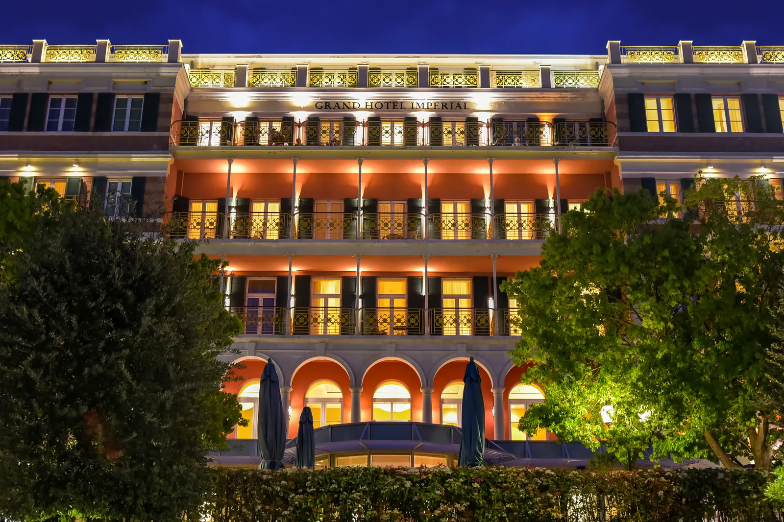 Verlichte gevel van het Grand Hotel Imperial (Hilton) in Dubrovnik bij avond, omringd door groen