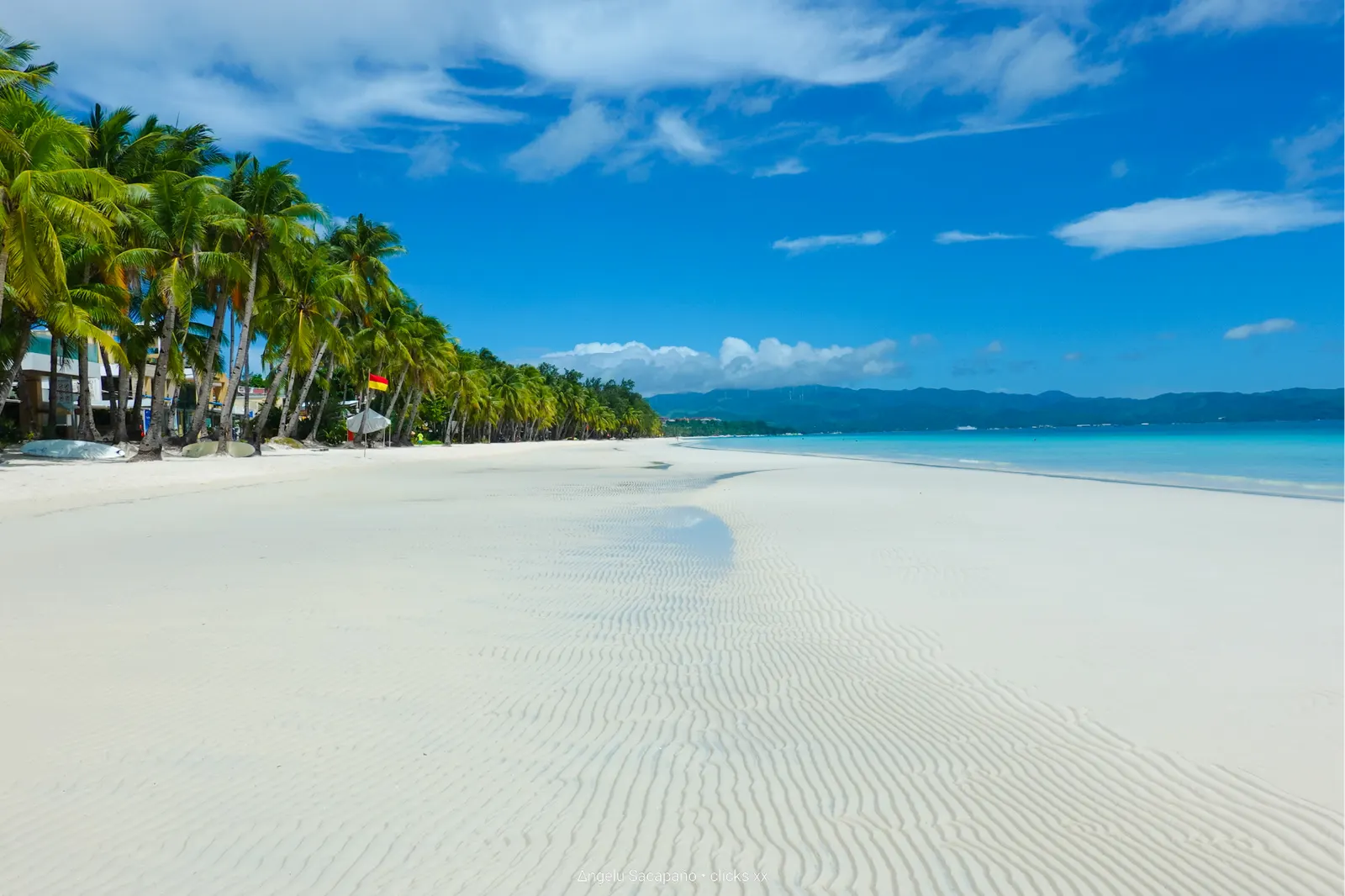 Wit zandstrand met palmbomen en turquoise zee onder een blauwe lucht op Boracay
