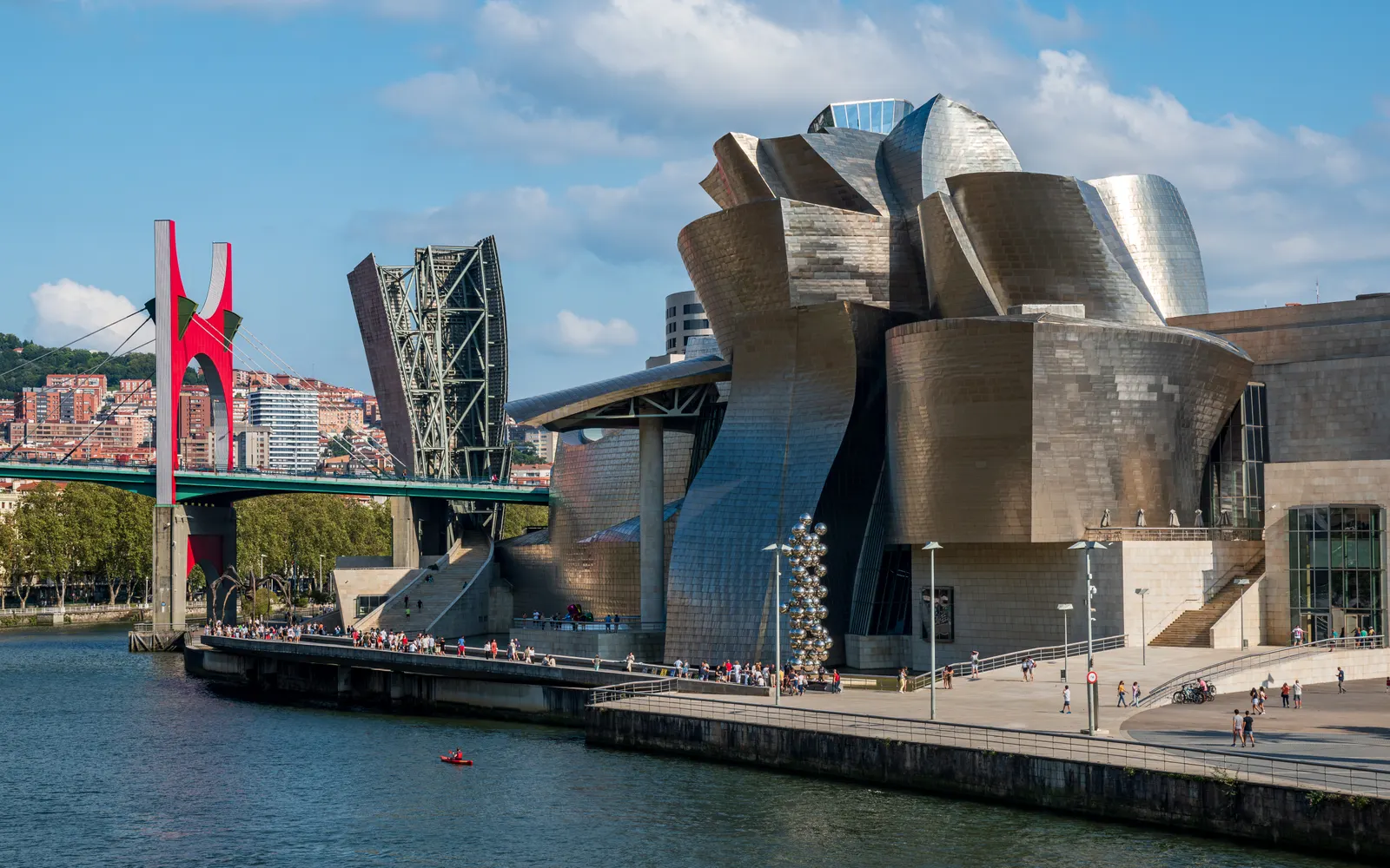 Guggenheim Museum Bilbao met titanium gevel aan de rivier, met de rode La Salve-brug en blauwe lucht
