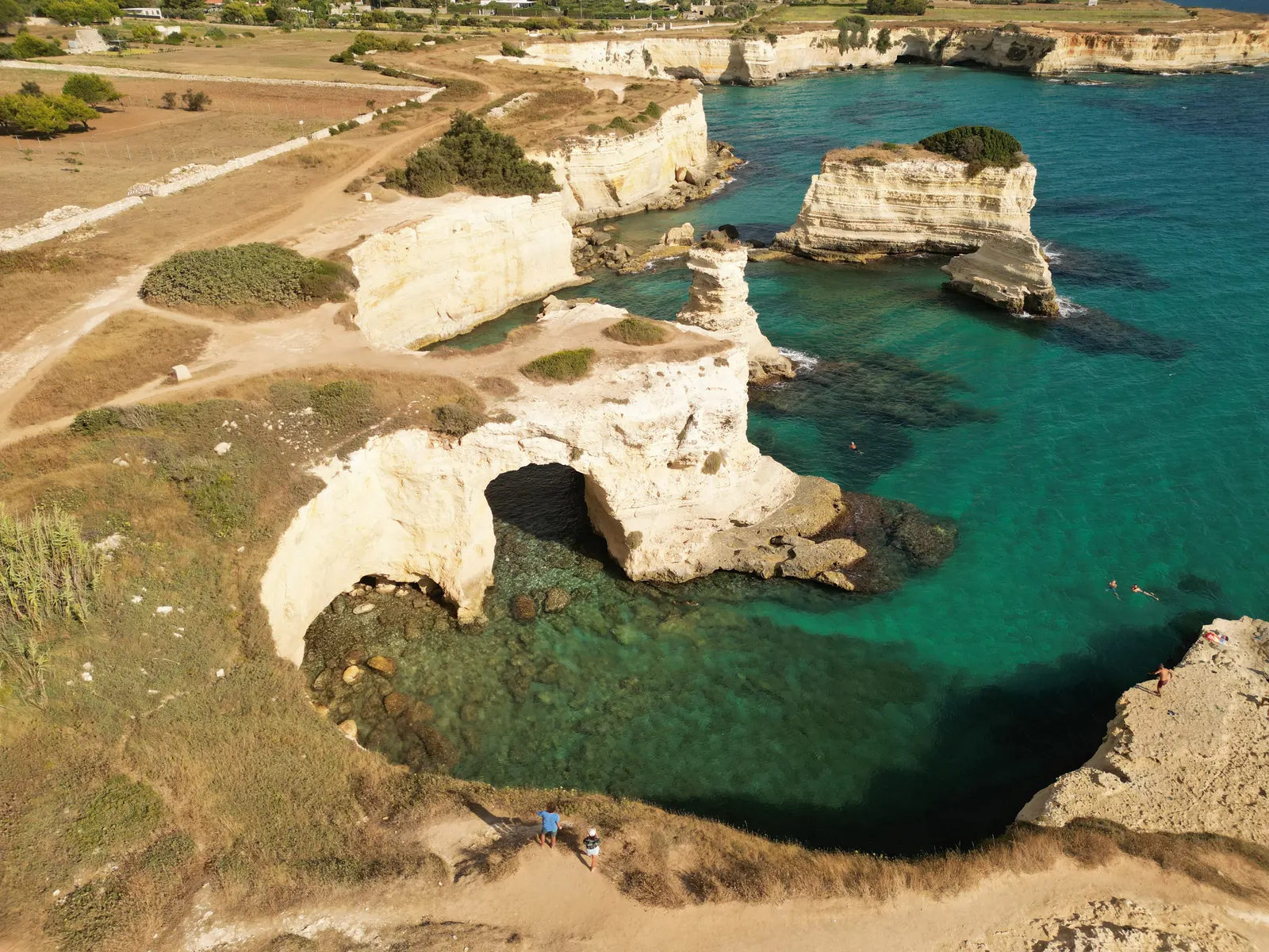 Luchtfoto van witte kalkstenen kliffen, rotsboog en faraglioni in turquoise zee bij Torre Sant'Andrea