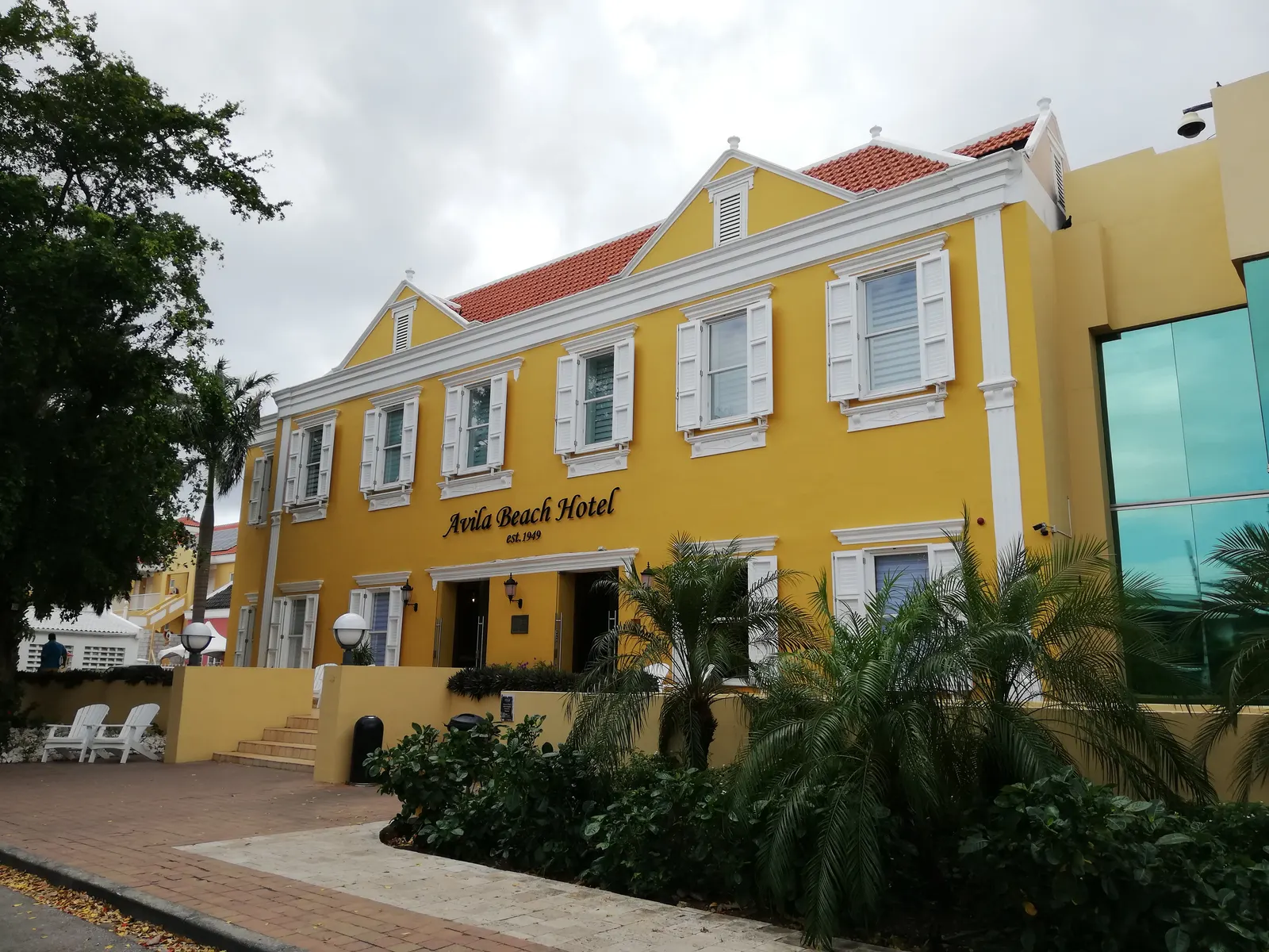Geel koloniaal gebouw van het Avila Beach Hotel met witte luiken en palmen in Willemstad
