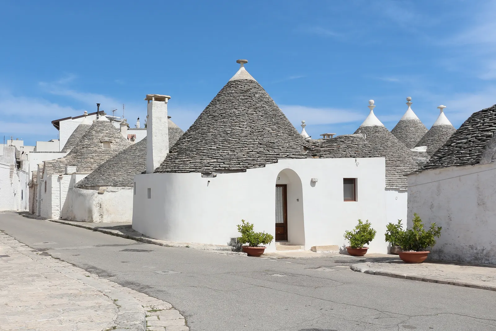 Witgekalkte trulli met kegelvormige stenen daken aan een zonnige straat in Alberobello onder een blauwe lucht
