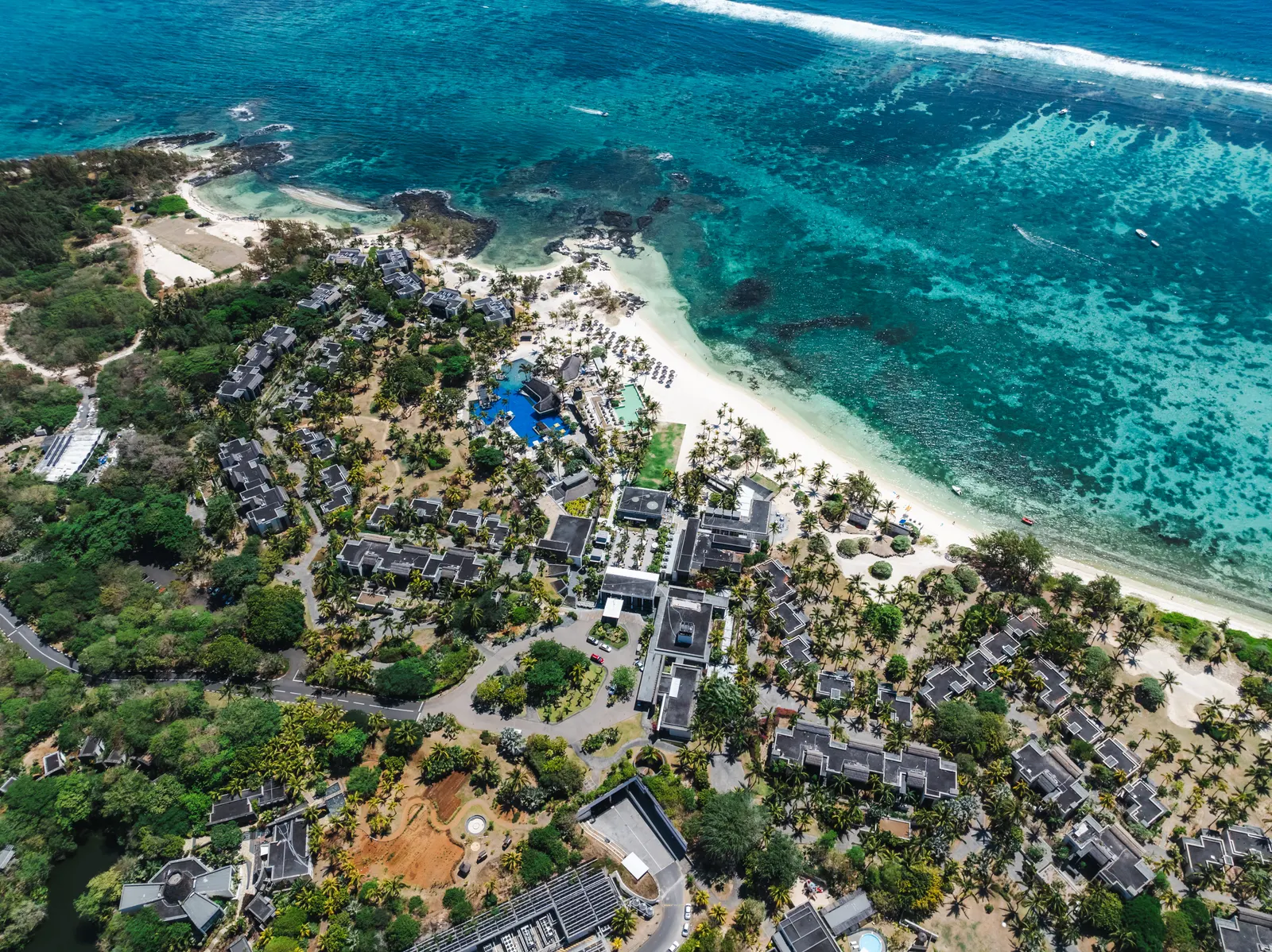 Luchtfoto van een luxe resort met villa's, zwembad en wit strand aan een turquoise lagune op Mauritius