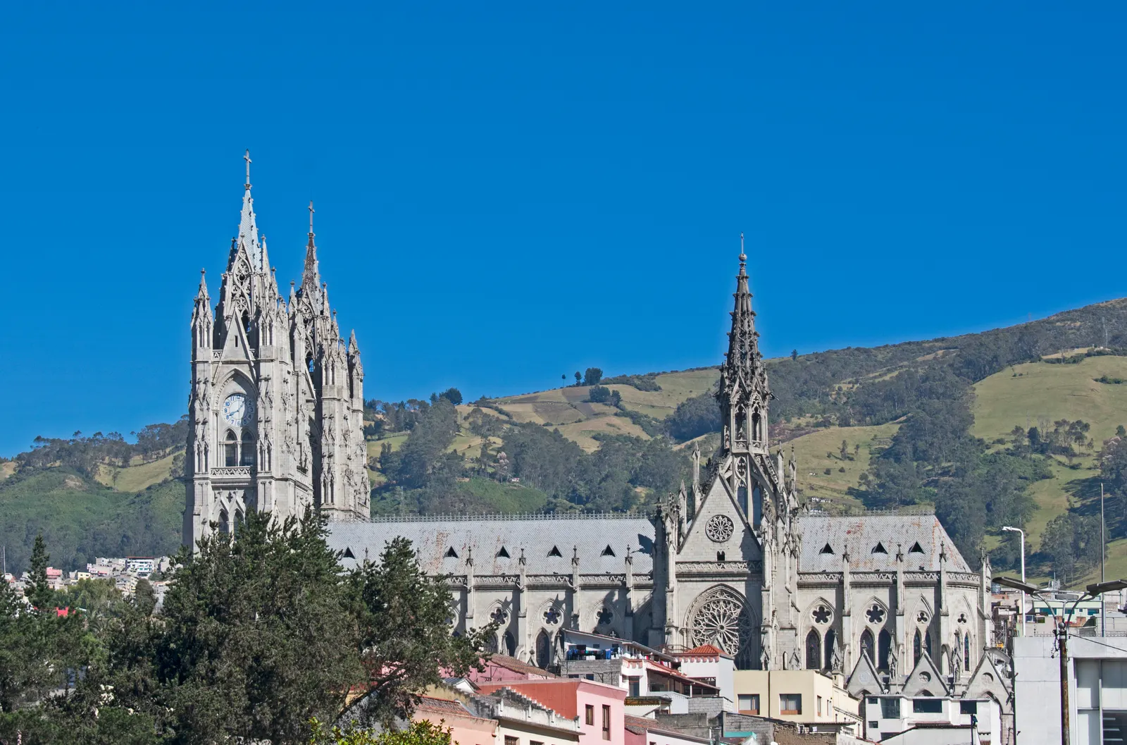 Neogotische Basílica del Voto Nacional met hoge torens tegen een strakblauwe lucht en groene heuvels in Quito