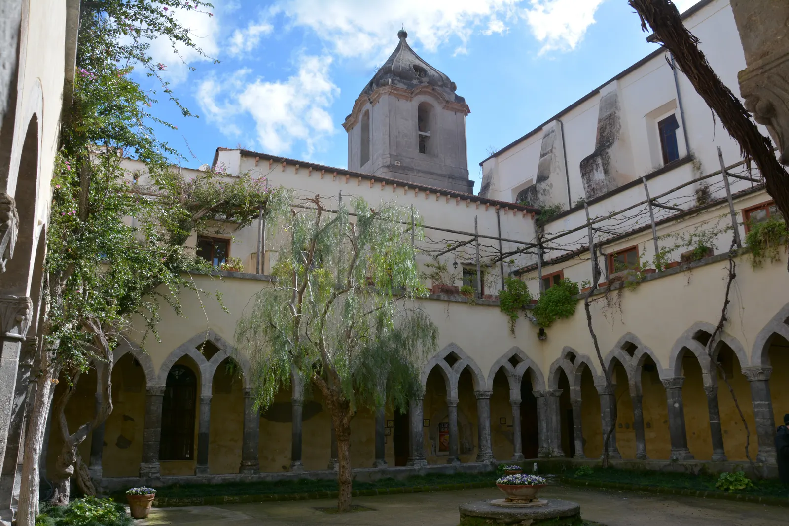 Kloostergang van San Francesco in Sorrento met spitsbogen, binnenplaats met boom en klokkentoren tegen blauwe lucht