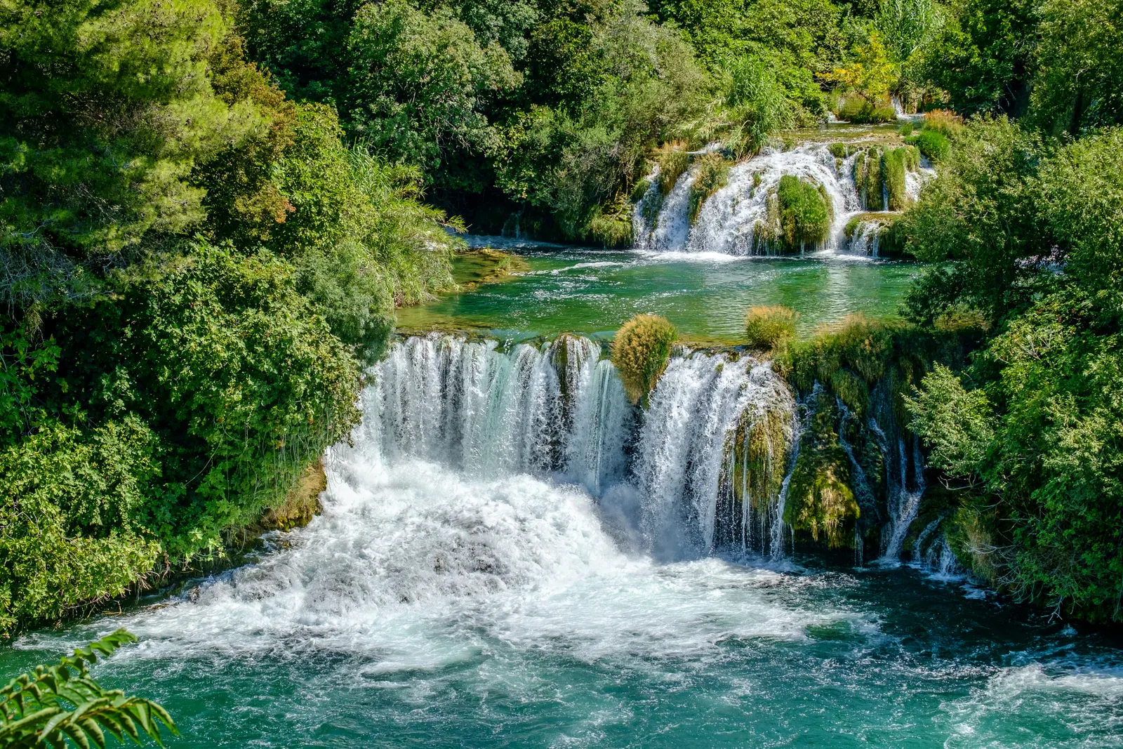 Trapsgewijze watervallen met turquoise water tussen groene bomen in Nationaal Park Krka