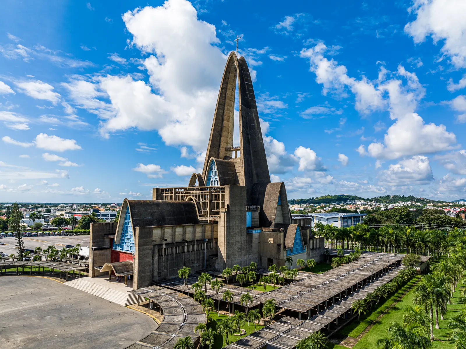 Luchtfoto van de Basiliek van Higüey met haar hoge betonnen boog, palmbomen en blauwe lucht met wolken