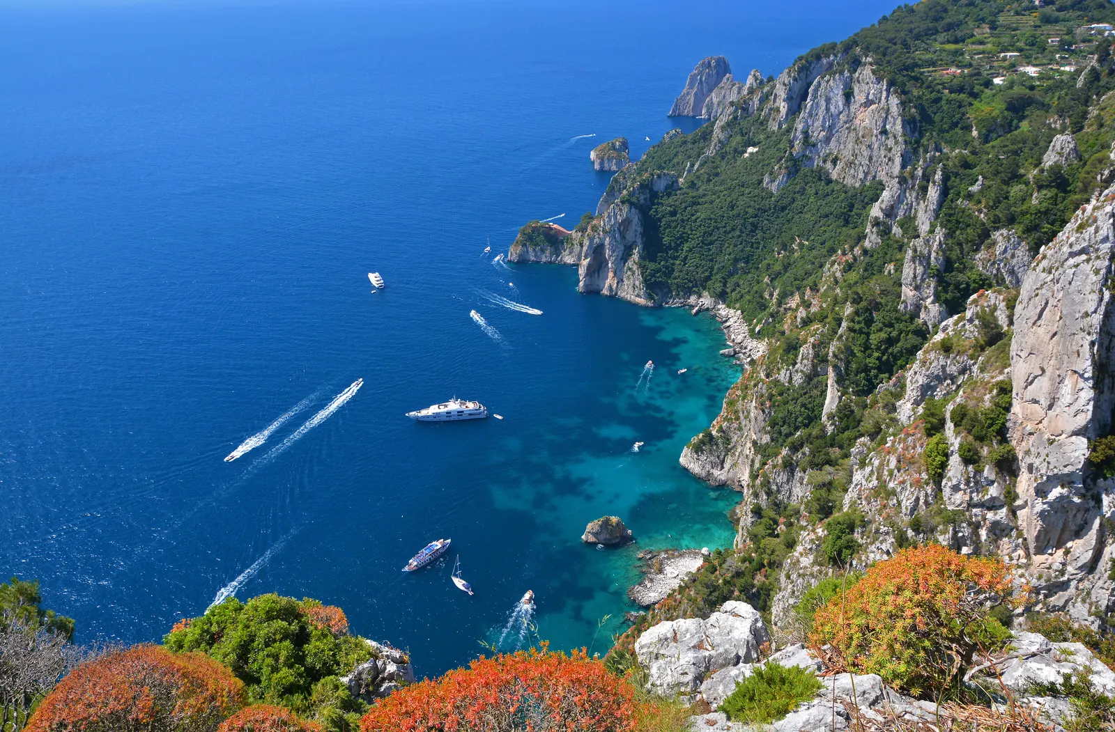 Steile rotskust van Capri met turquoise baaien en boten op diepblauwe zee, gezien vanaf een hoog uitzichtpunt