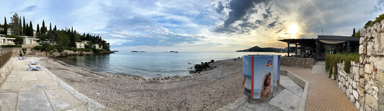 Panorama van het kiezelstrand van Mlini met palmen, ligstoelen en zonsondergang boven de Adriatische Zee