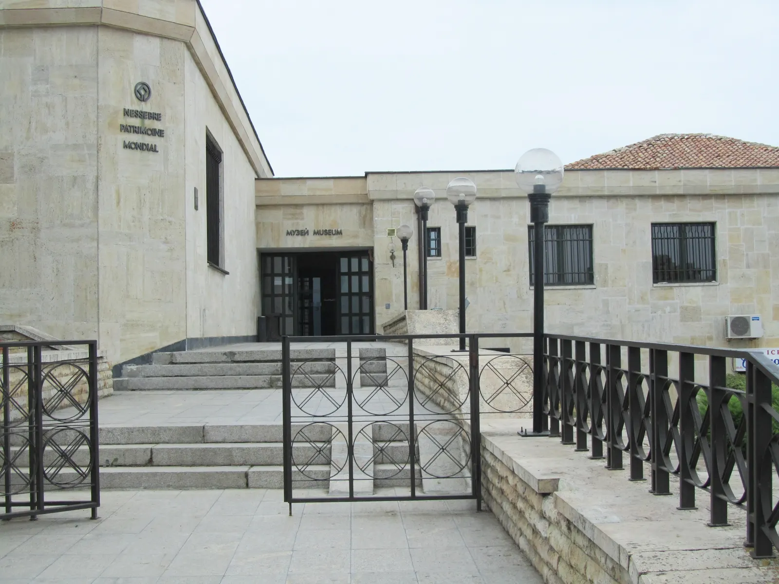 Ingang van het Archeologisch Museum van Nessebar, een lichtstenen gebouw met trappen en een zwart hek