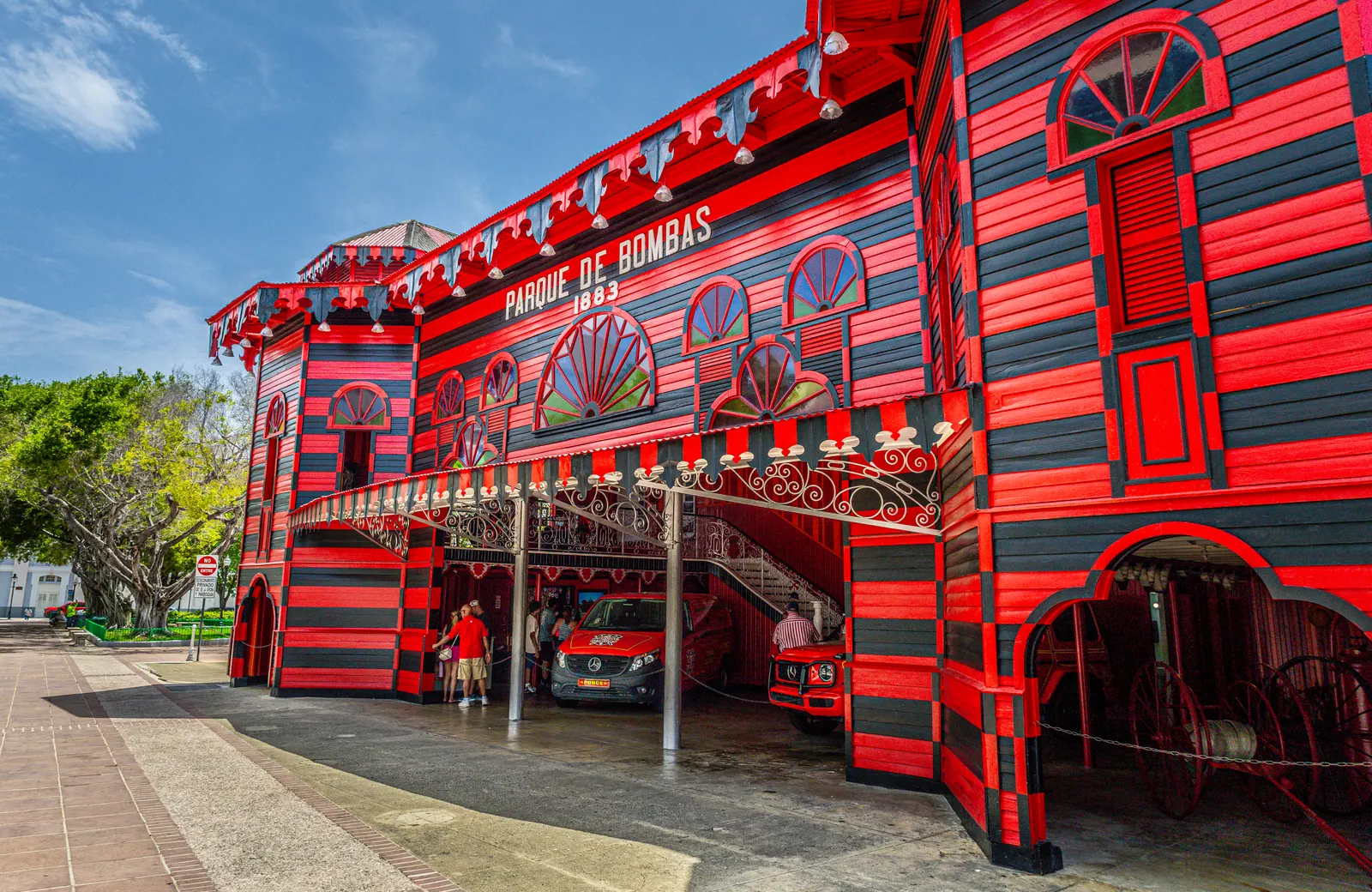 Het rood-zwart gestreepte Parque de Bombas in Ponce onder een blauwe lucht, met het opschrift 'Parque de Bombas 1883'