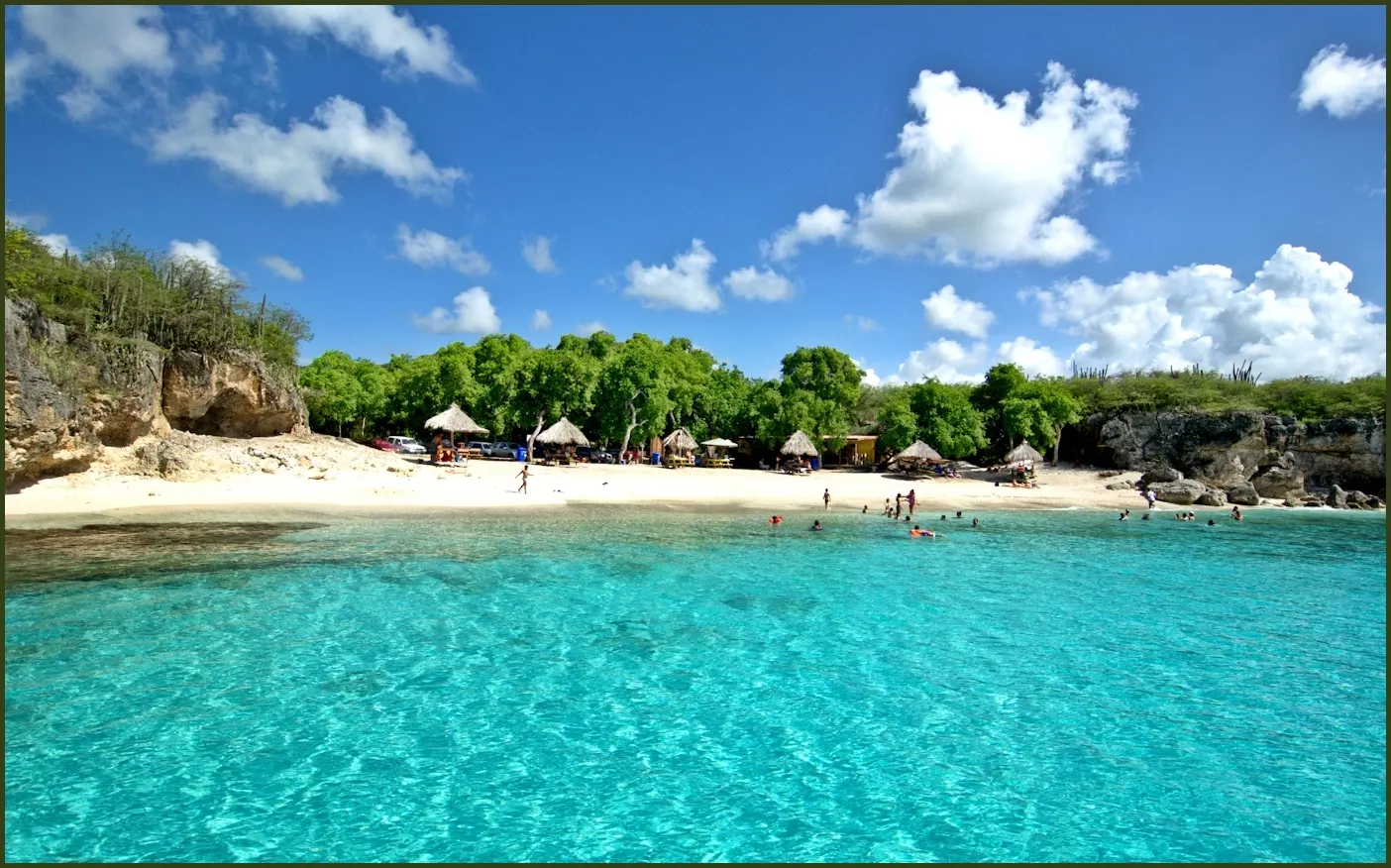 Turquoise water en wit zandstrand met parasols van Kleine Knip, omringd door rotsen en groen