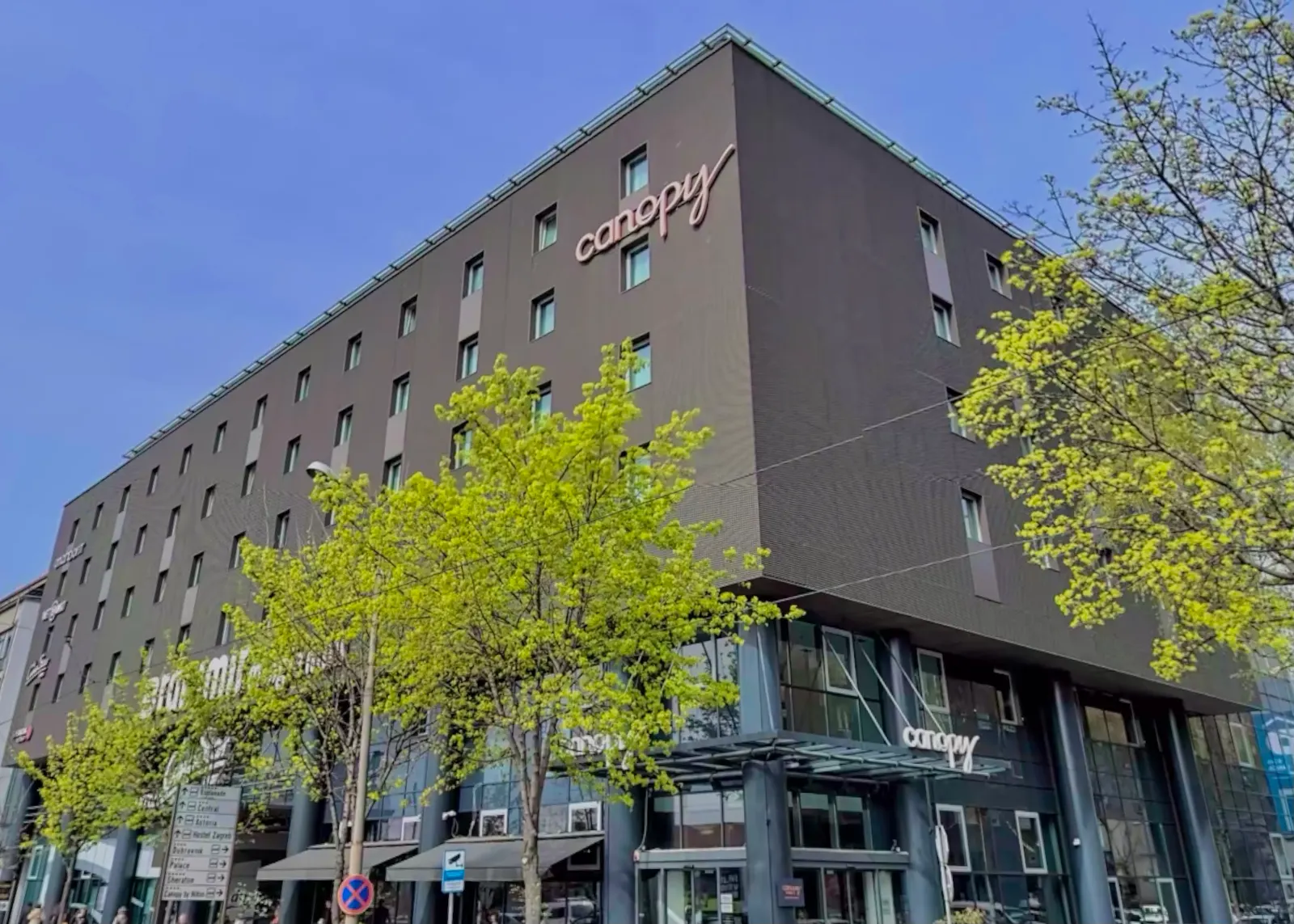 Modern hotelgebouw van Canopy by Hilton in Zagreb met groene bomen ervoor onder een blauwe lucht