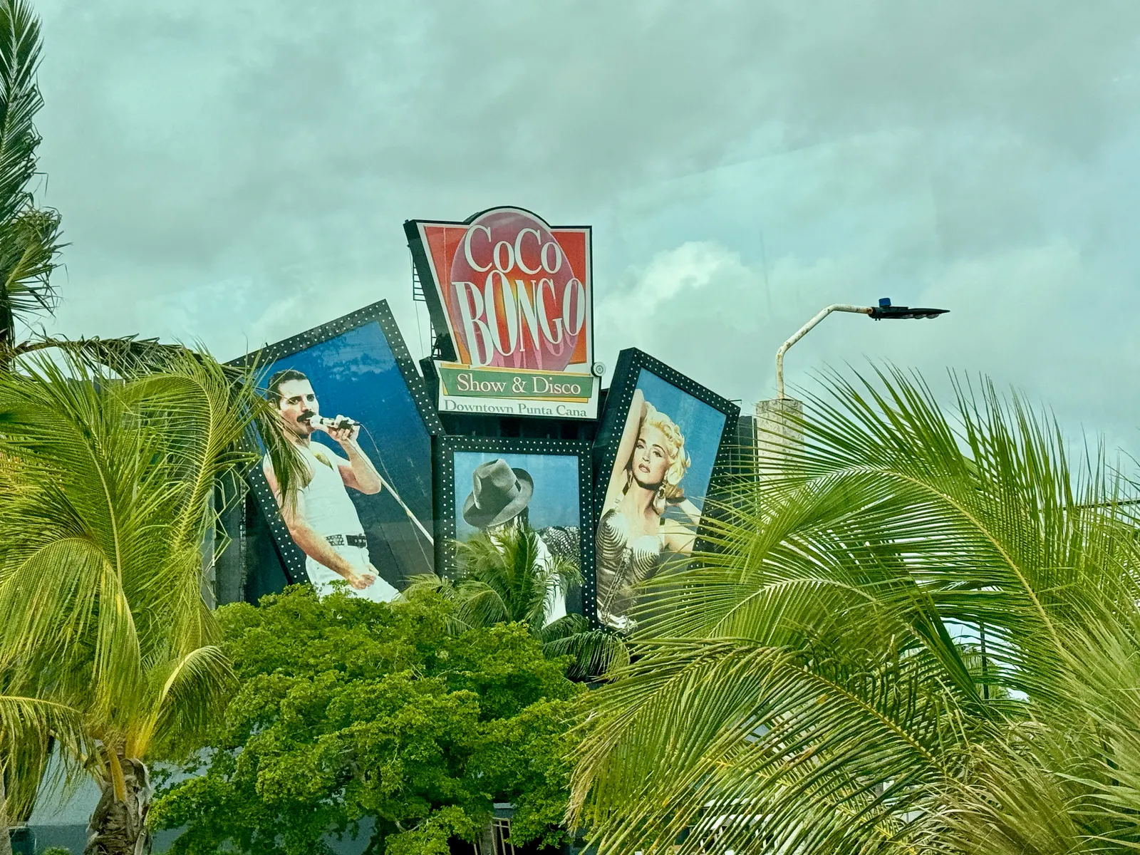 Reclamebord van Coco Bongo Show & Disco in Punta Cana tussen palmbomen onder een bewolkte lucht