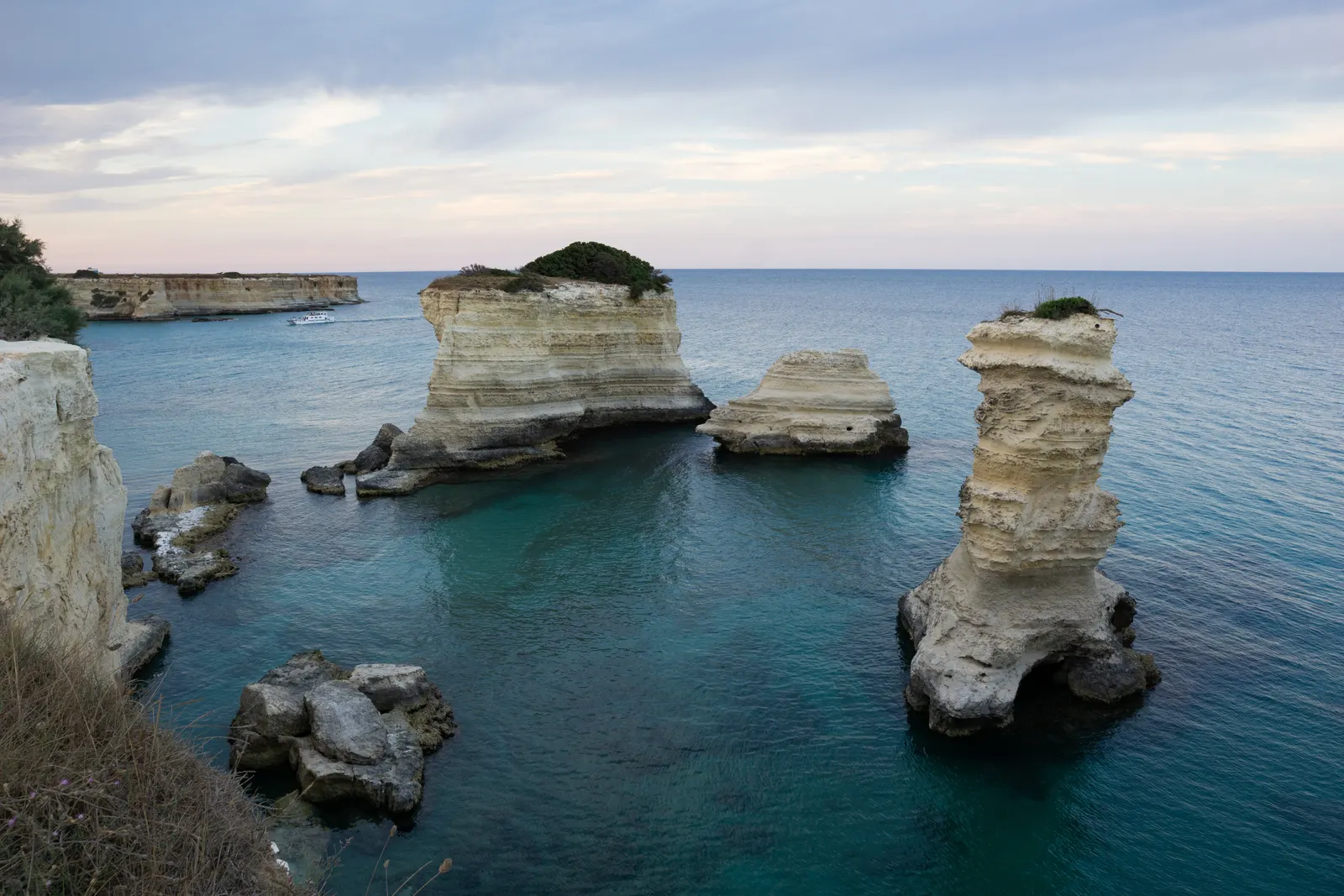 Witte kalkstenen zeestapels in turquoise water langs de rotskust van Torre Sant'Andrea