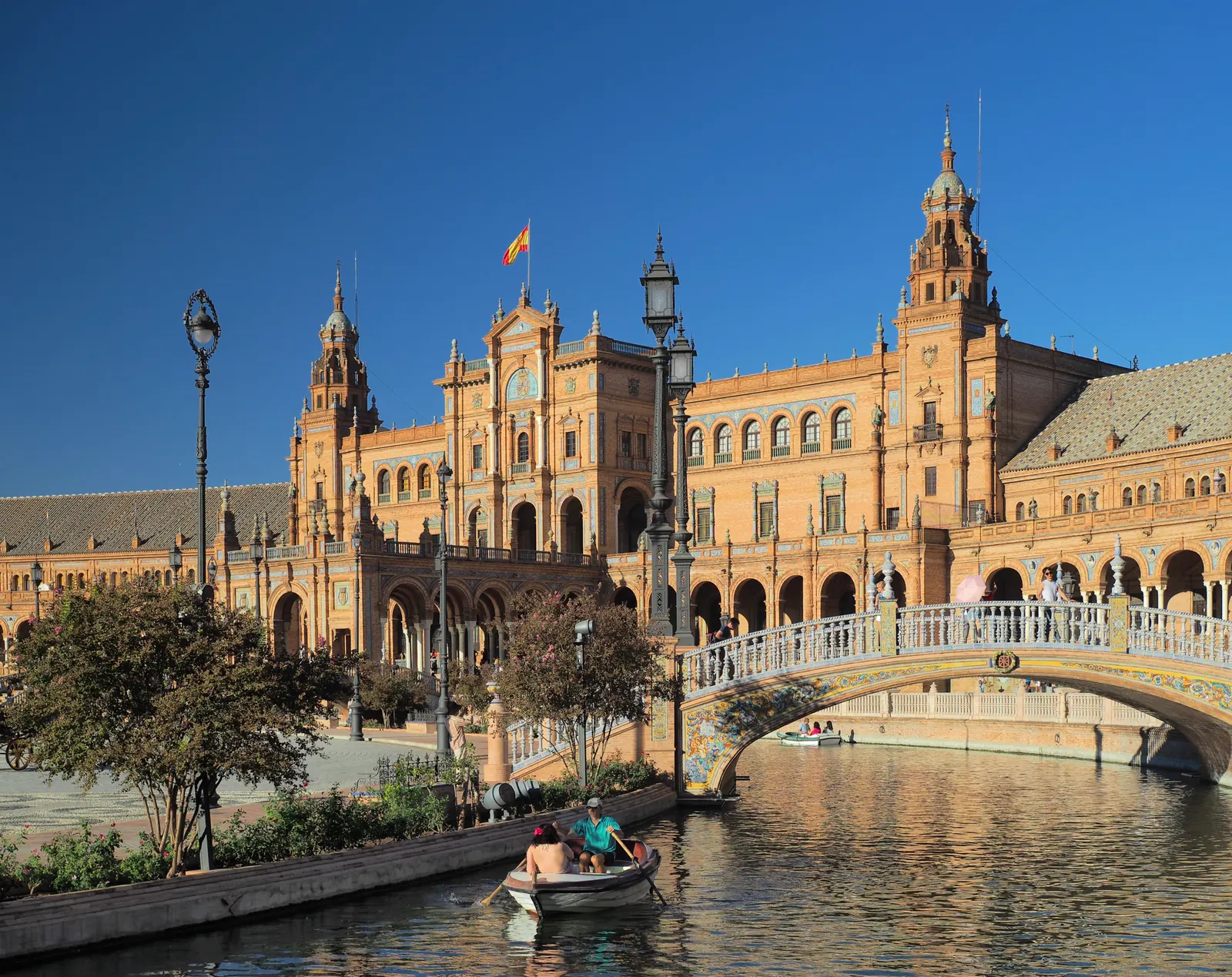 Plaza de España in Sevilla met roeiboot op het kanaal, sierlijke brug en torens onder een strakblauwe lucht