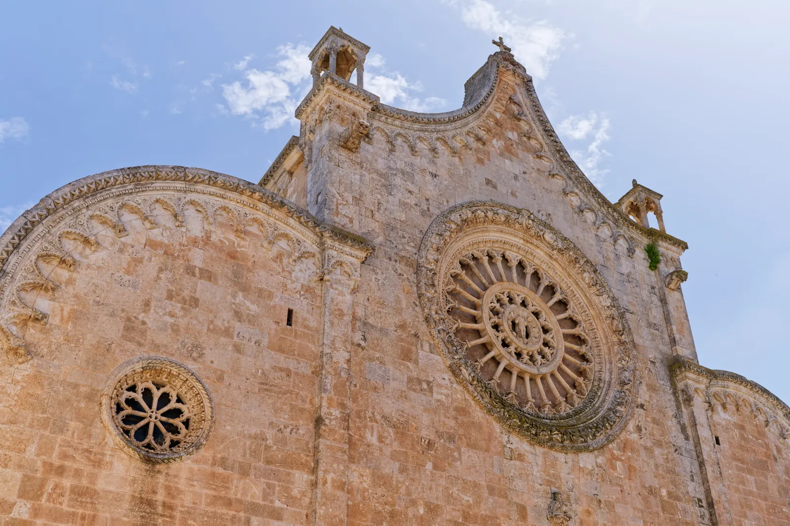 Gotische gevel van de kathedraal van Ostuni met groot roosvenster en gebogen topgevel tegen een blauwe lucht