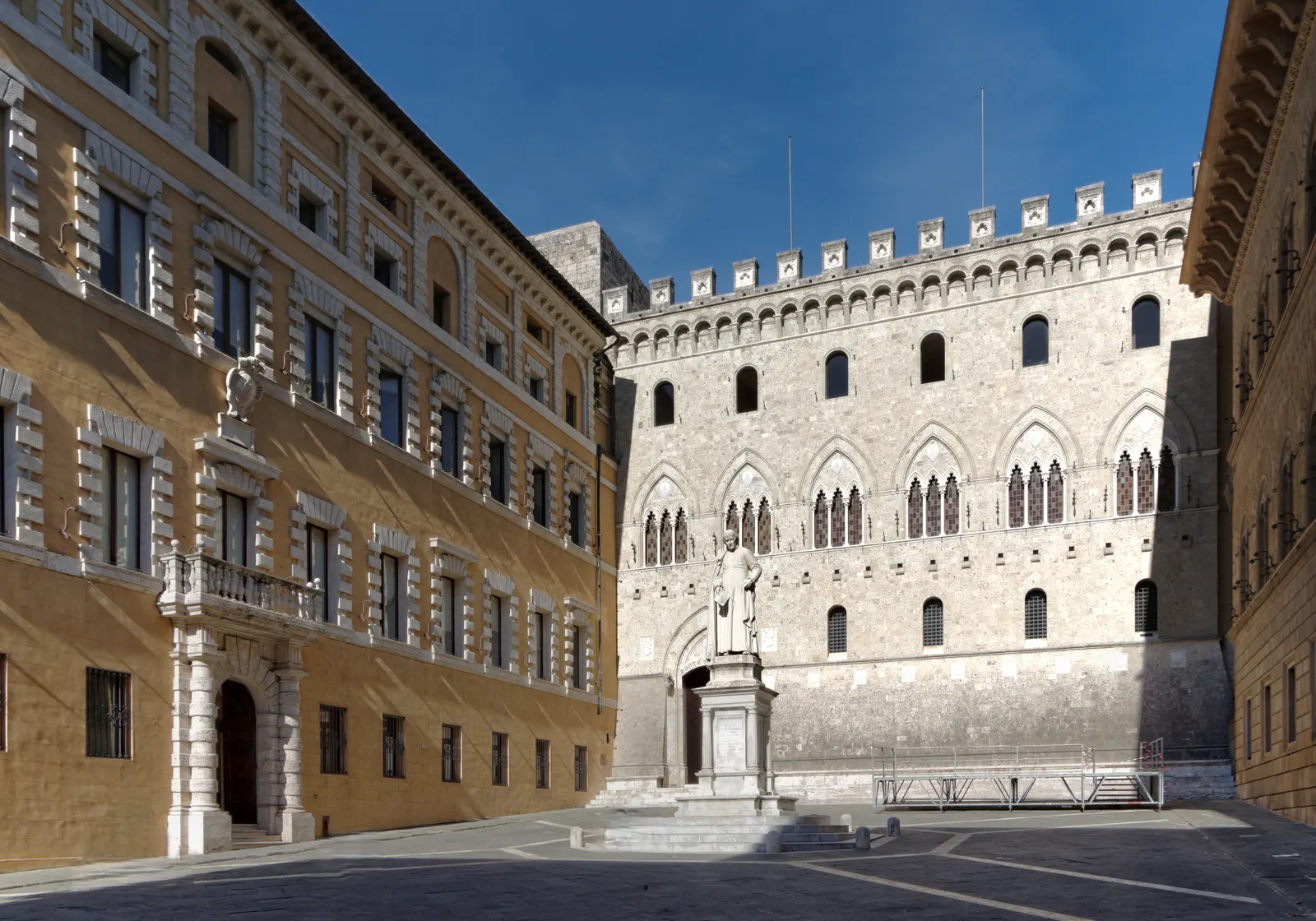 Piazza Salimbeni in Siena met het gotische Palazzo Salimbeni en het standbeeld van Sallustio Bandini onder blauwe lucht