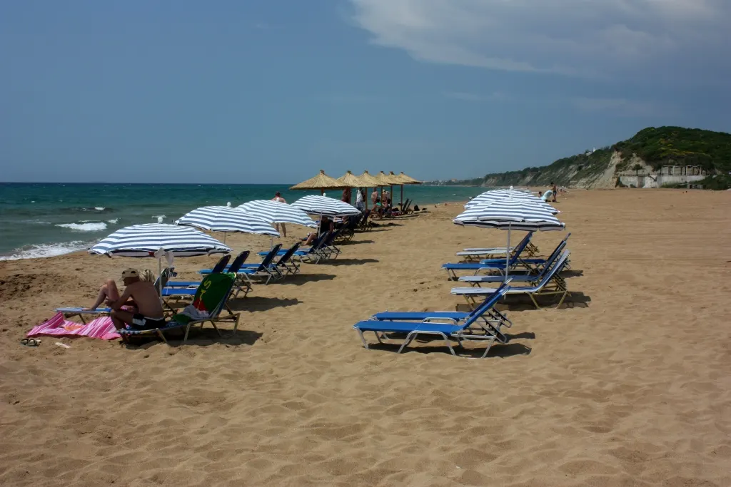 Breed zandstrand van Marathias met blauwe ligbedden, parasols en groene kliffen langs de zee