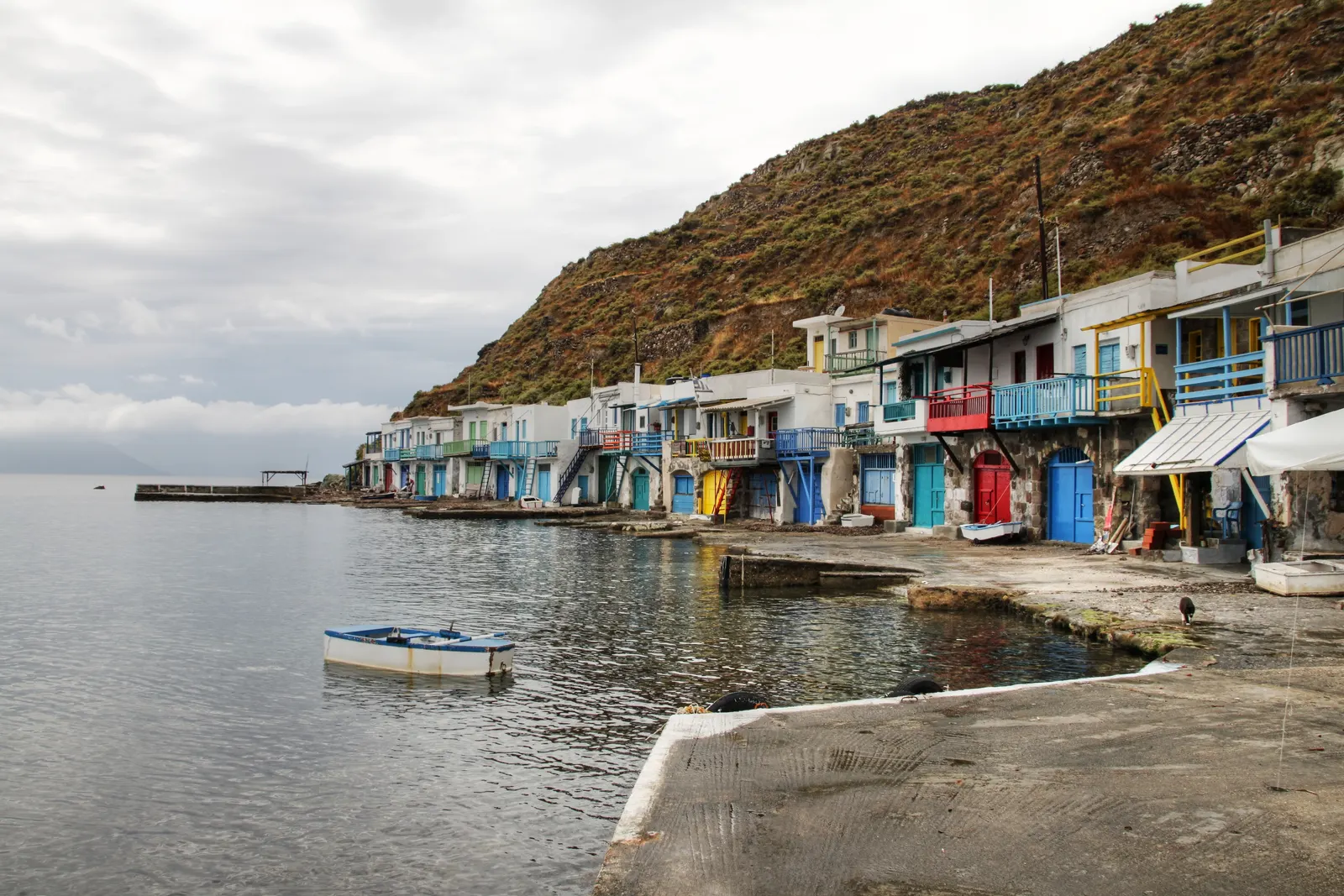 Kleurrijke vissershuisjes (syrmata) aan het water in Klima op Milos, met een bootje en een heuvel erachter