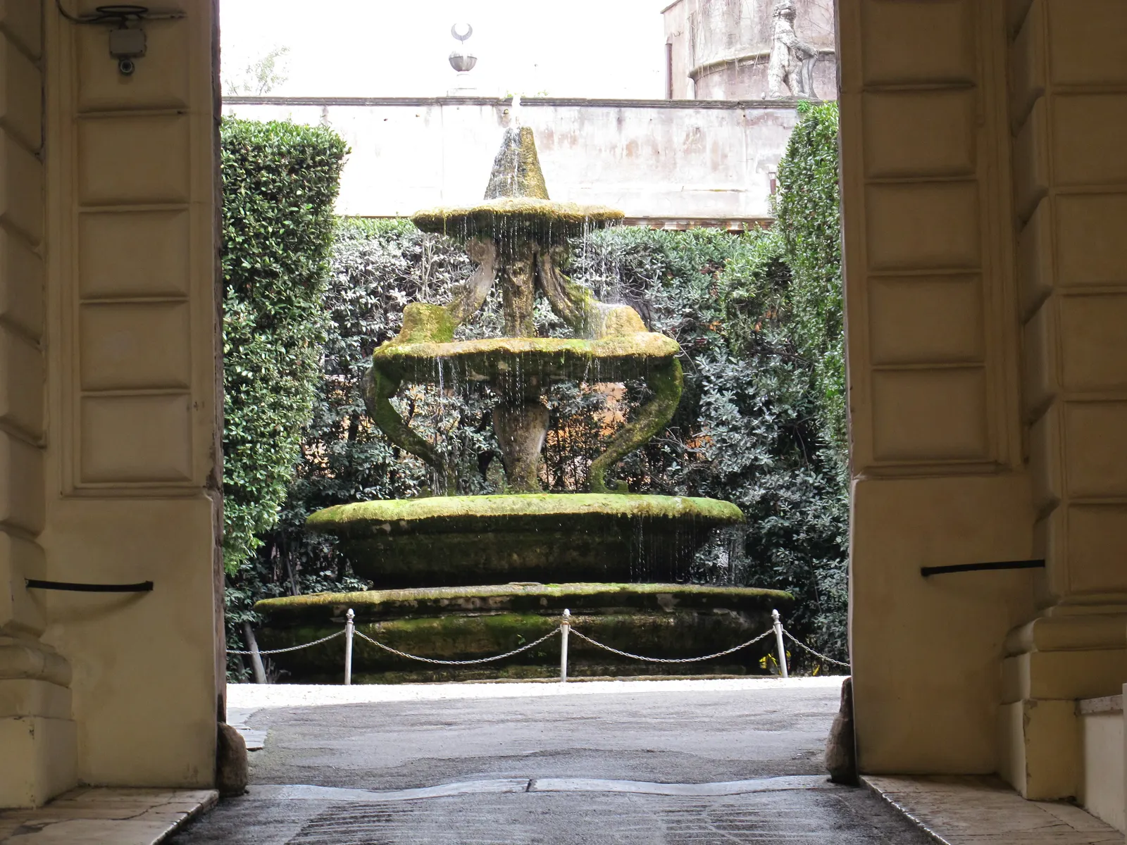 Met mos begroeide fontein op de binnenplaats van Palazzo Taverna in Rome, gezien door de toegangspoort