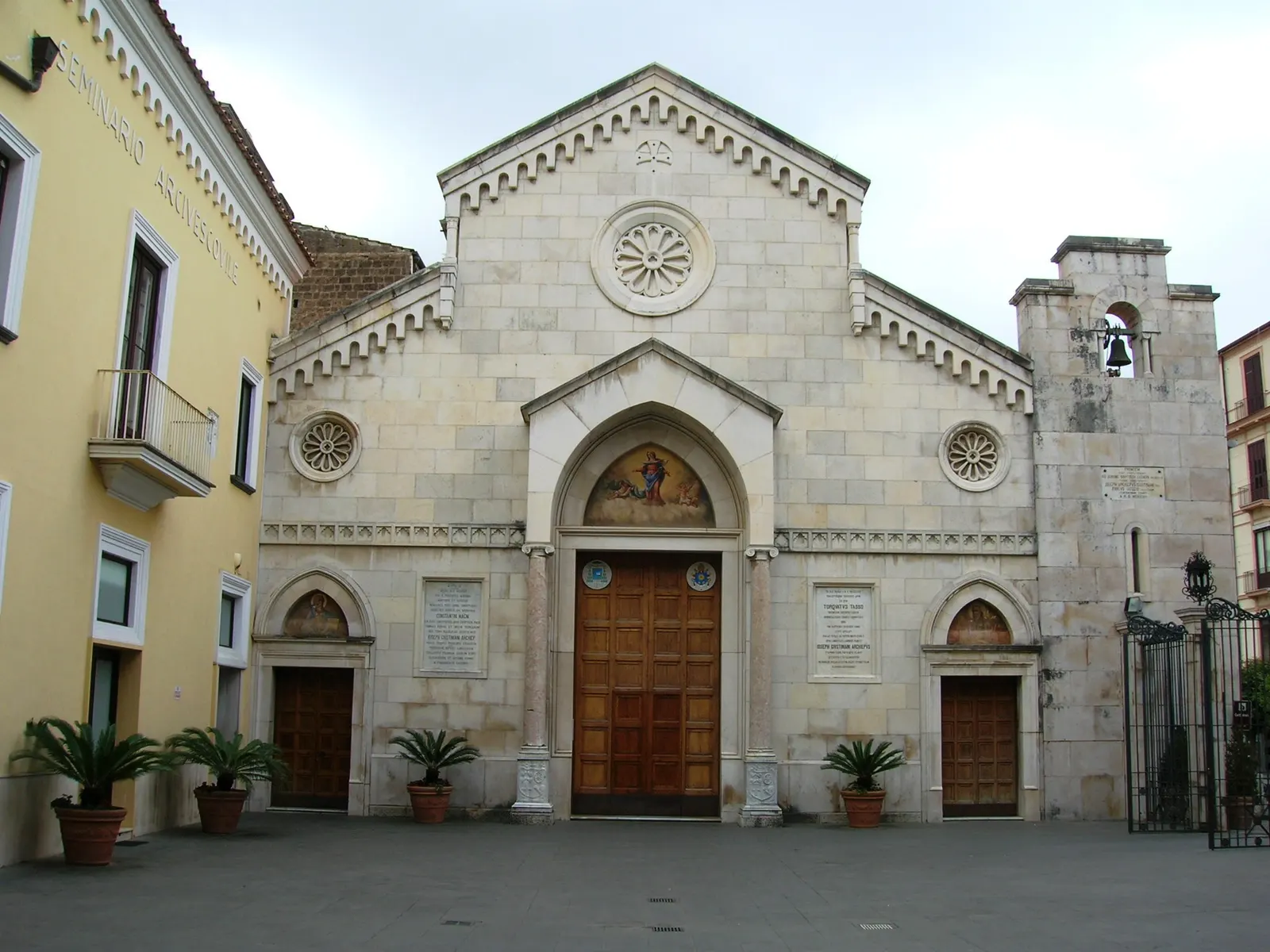 Lichtstenen gevel van de kathedraal van Sorrento met houten deur, roosvensters en klokkentoren