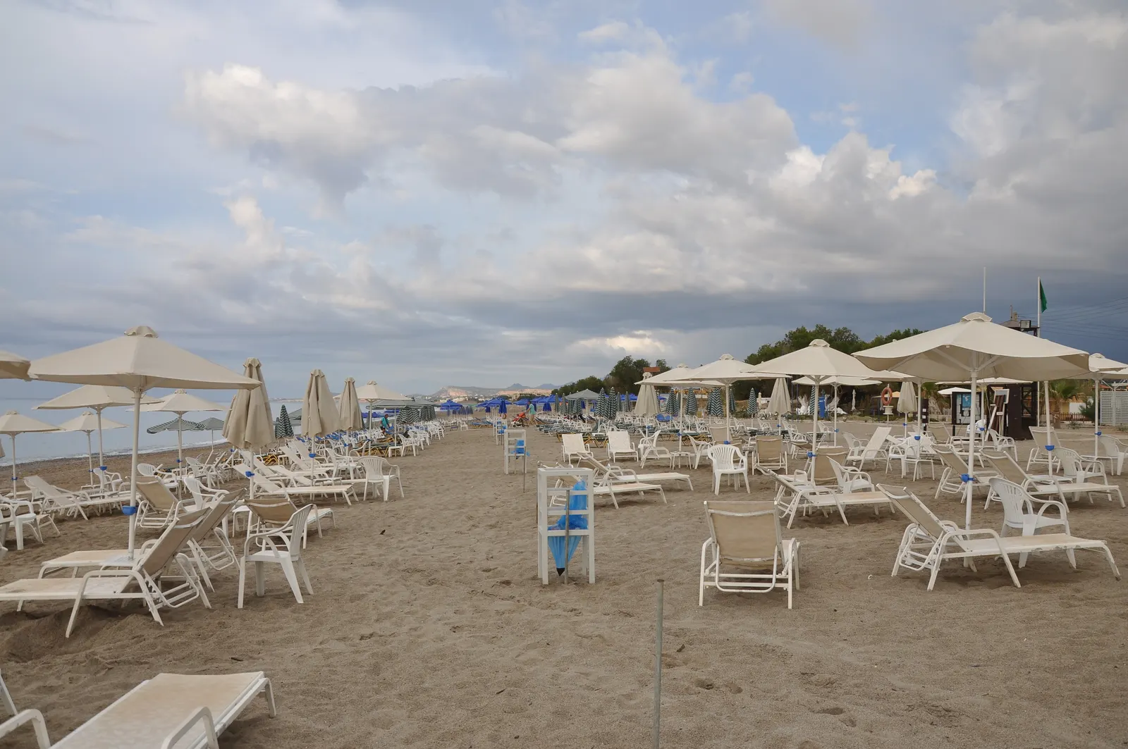 Breed zandstrand met rijen ligbedden en parasols onder een bewolkte lucht
