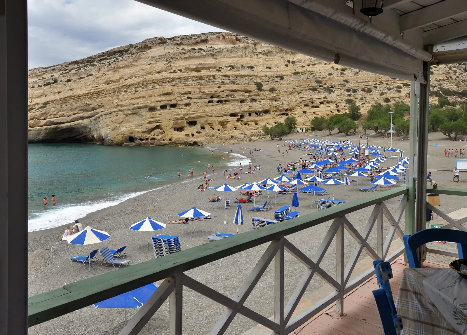 Uitzicht vanaf een terras over het strand van Matala met parasols en de rotswand vol grotten