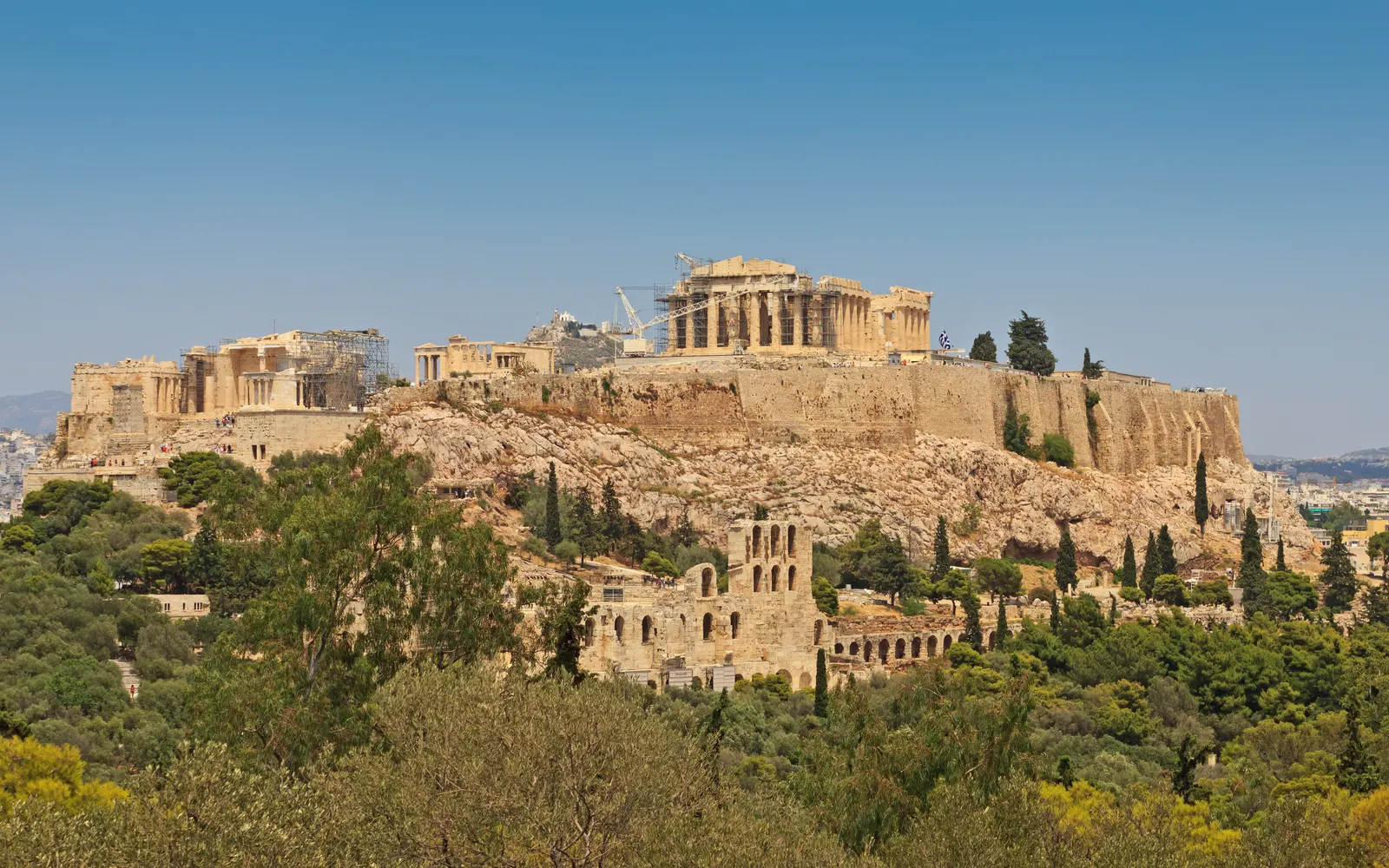 De Akropolis van Athene op de rotsheuvel met het Parthenon, omringd door groene bomen onder een blauwe lucht