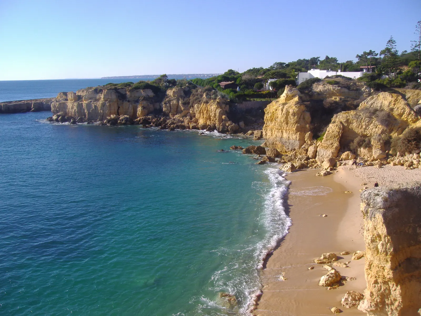 Turquoise zee en goudgele kliffen boven een klein zandstrand aan de kust bij Albufeira