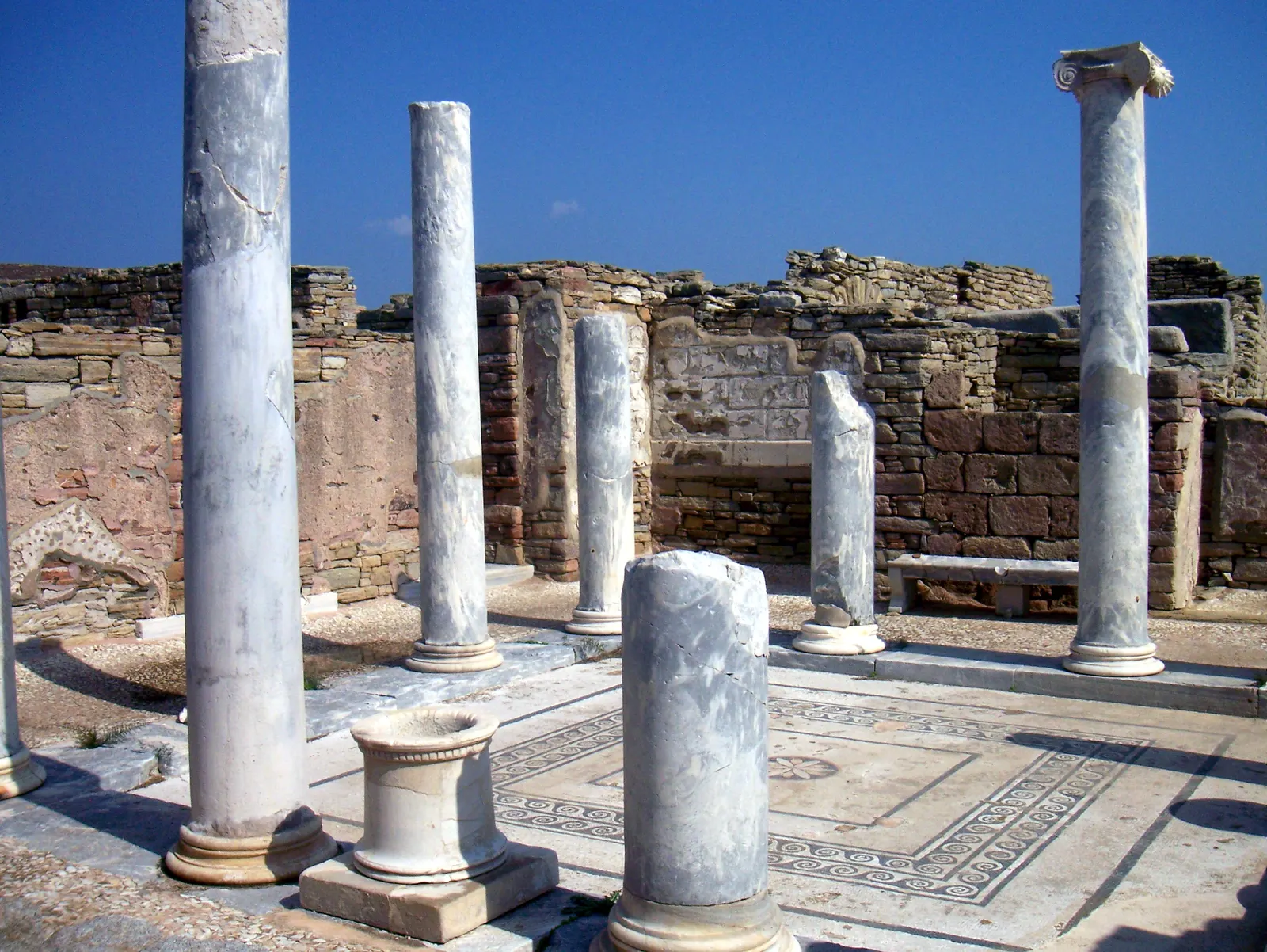 Marmeren zuilen rond een binnenplaats met mozaïekvloer in een antiek huis op Delos onder blauwe lucht