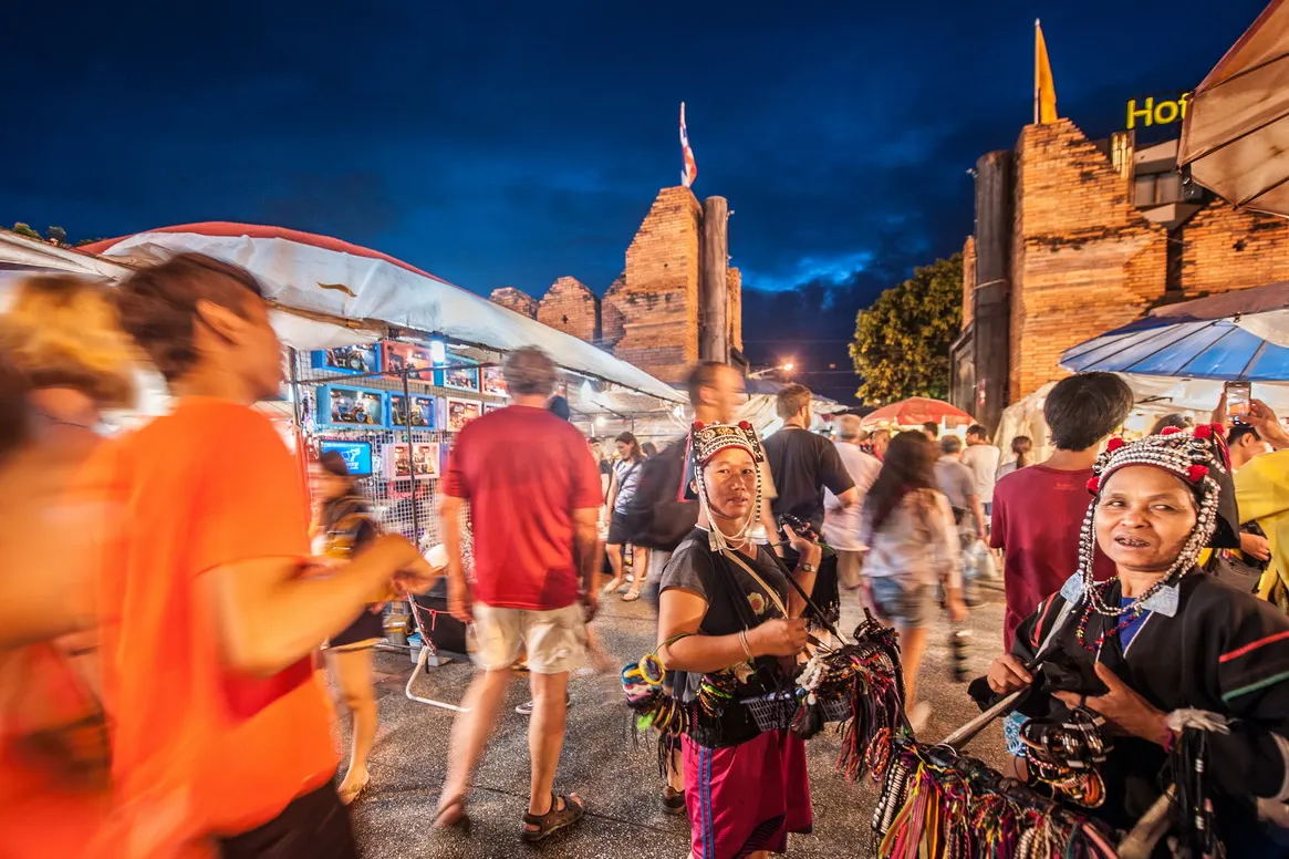 Drukke avondmarkt met kraampjes en verkoopsters in traditionele kleding bij de Tha Phae-poort in Chiang Mai