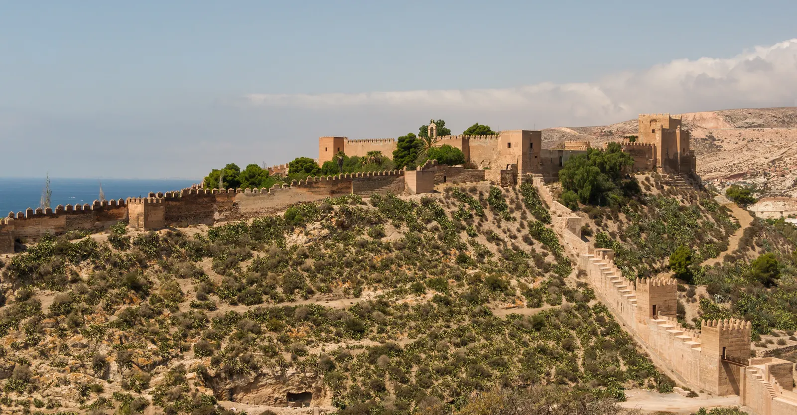 De Alcazaba van Almería met lange vestingmuren op een begroeide heuvel, met de zee op de achtergrond
