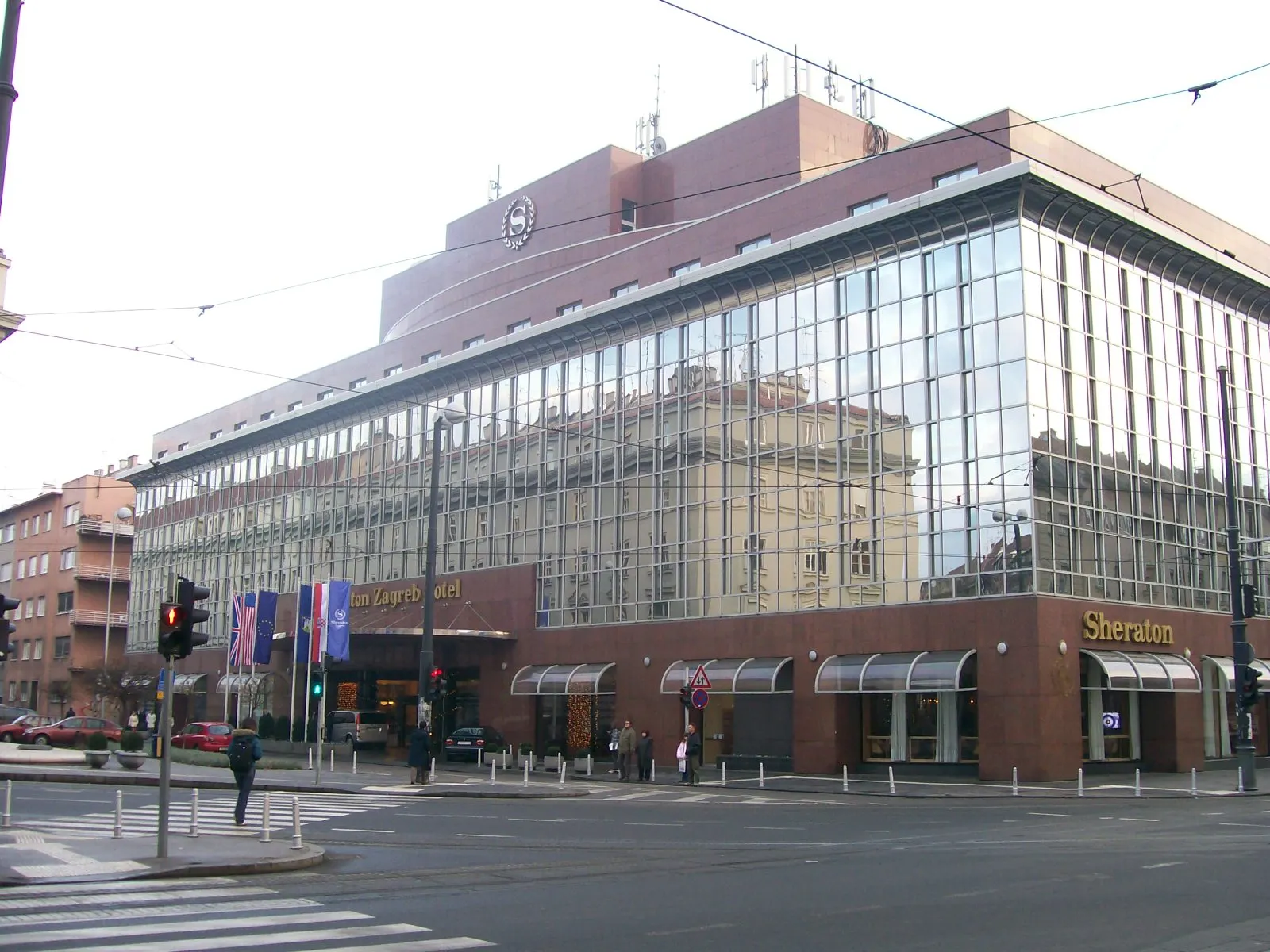 Glazen gevel van het Sheraton Zagreb Hotel op een straathoek met vlaggen bij de ingang